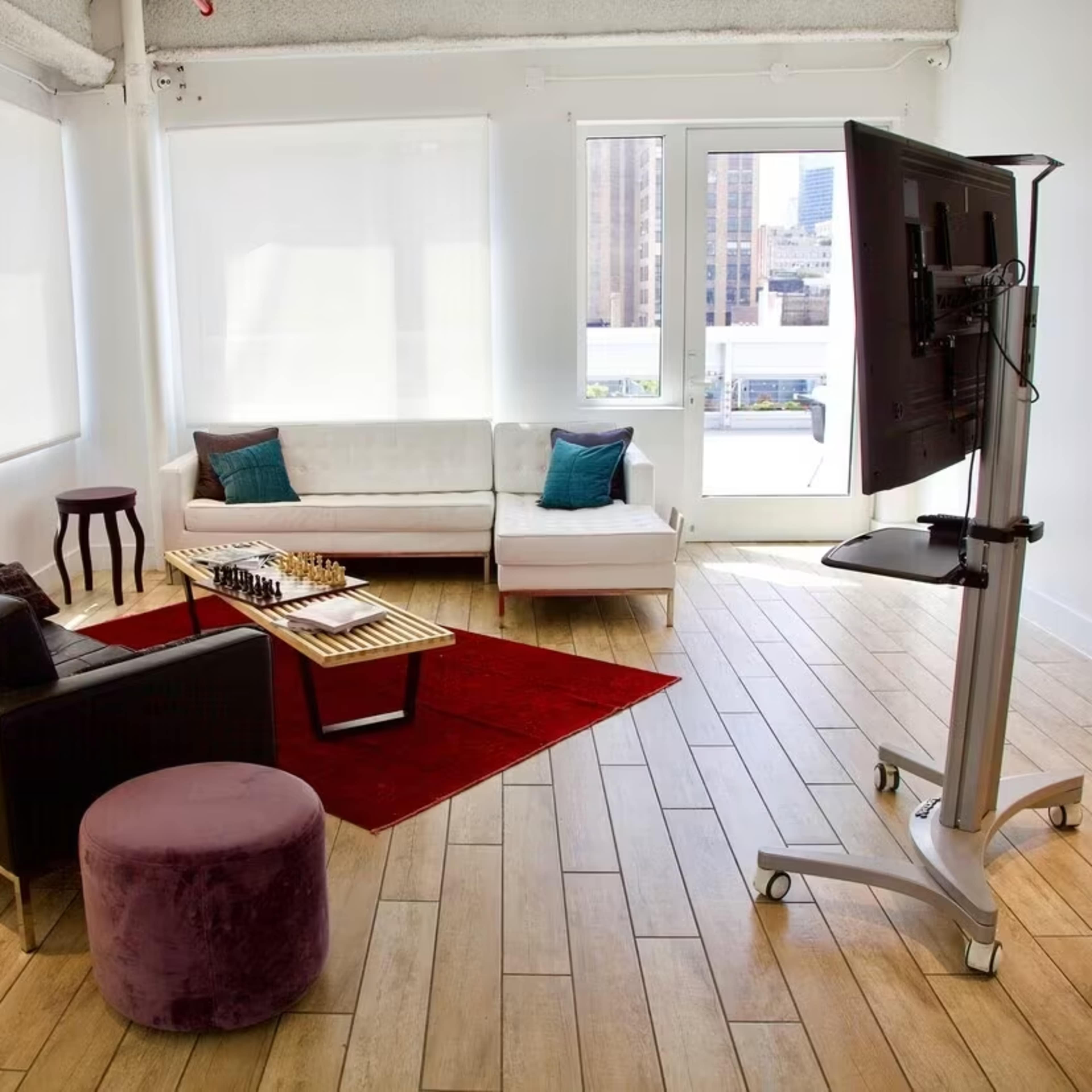 A minimalist living space with two sofas, a coffee table, a small side table, and a TV mounted on a stand, all set against a backdrop of large windows.