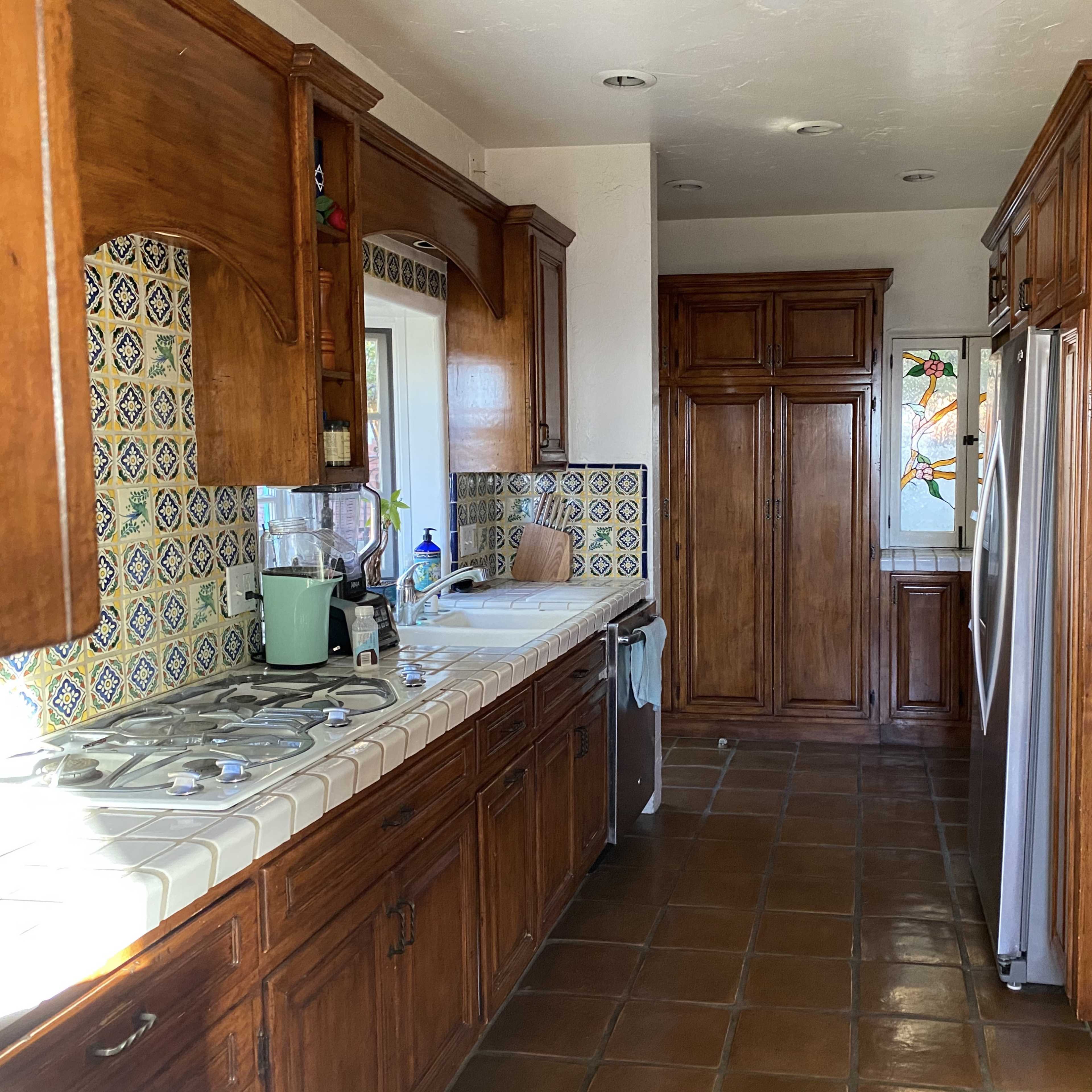 A kitchen with wooden cabinetry, tiled countertops, and a window featuring decorative glass.