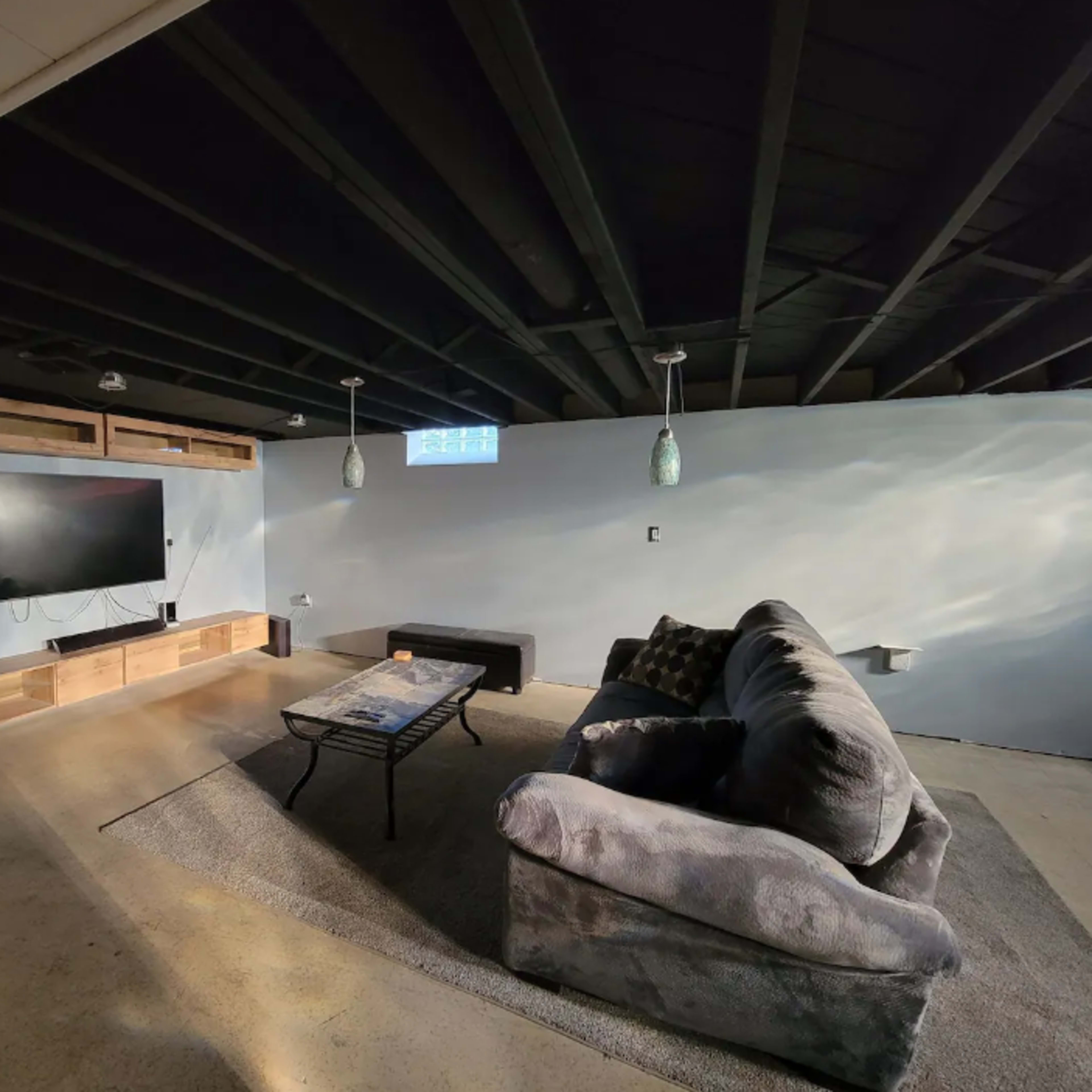 A basement living area featuring a large sofa, a coffee table, a wall-mounted television, and wooden shelves.