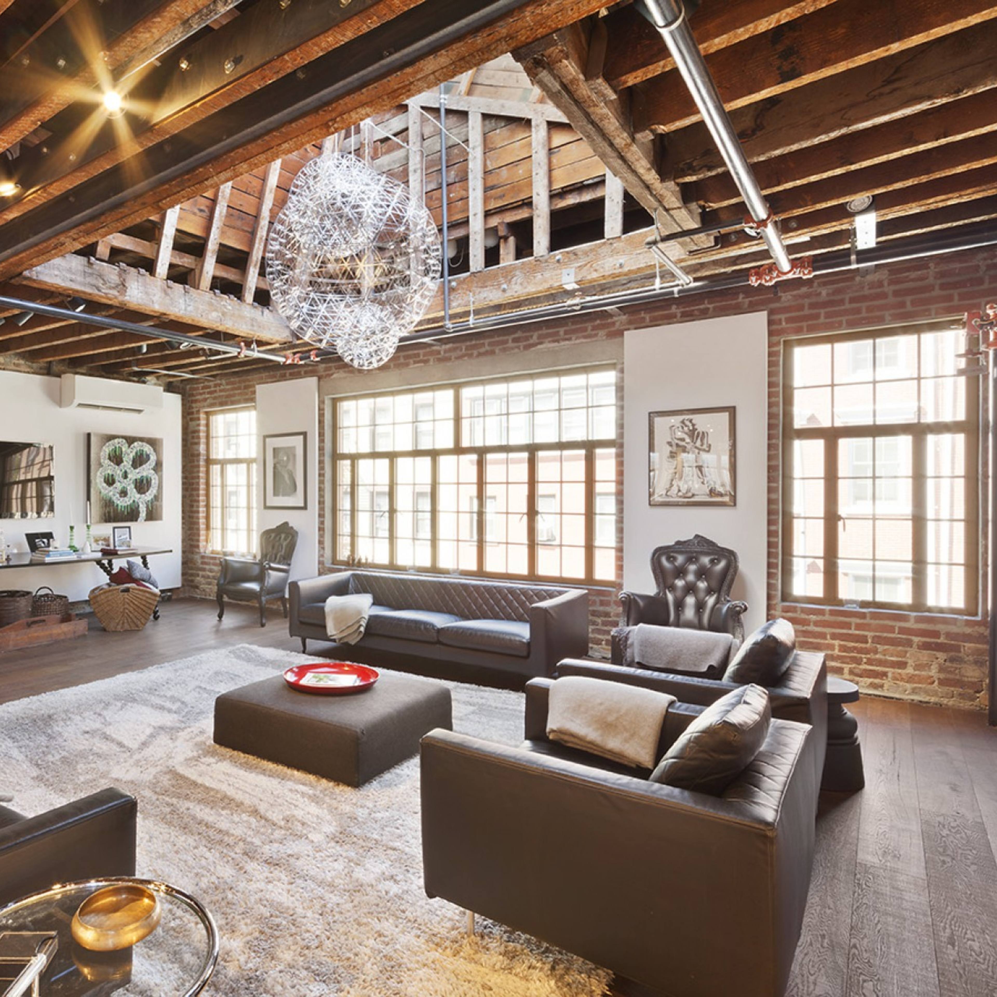 A spacious living room features exposed wooden beams, large windows, and modern furniture arranged around a central coffee table.