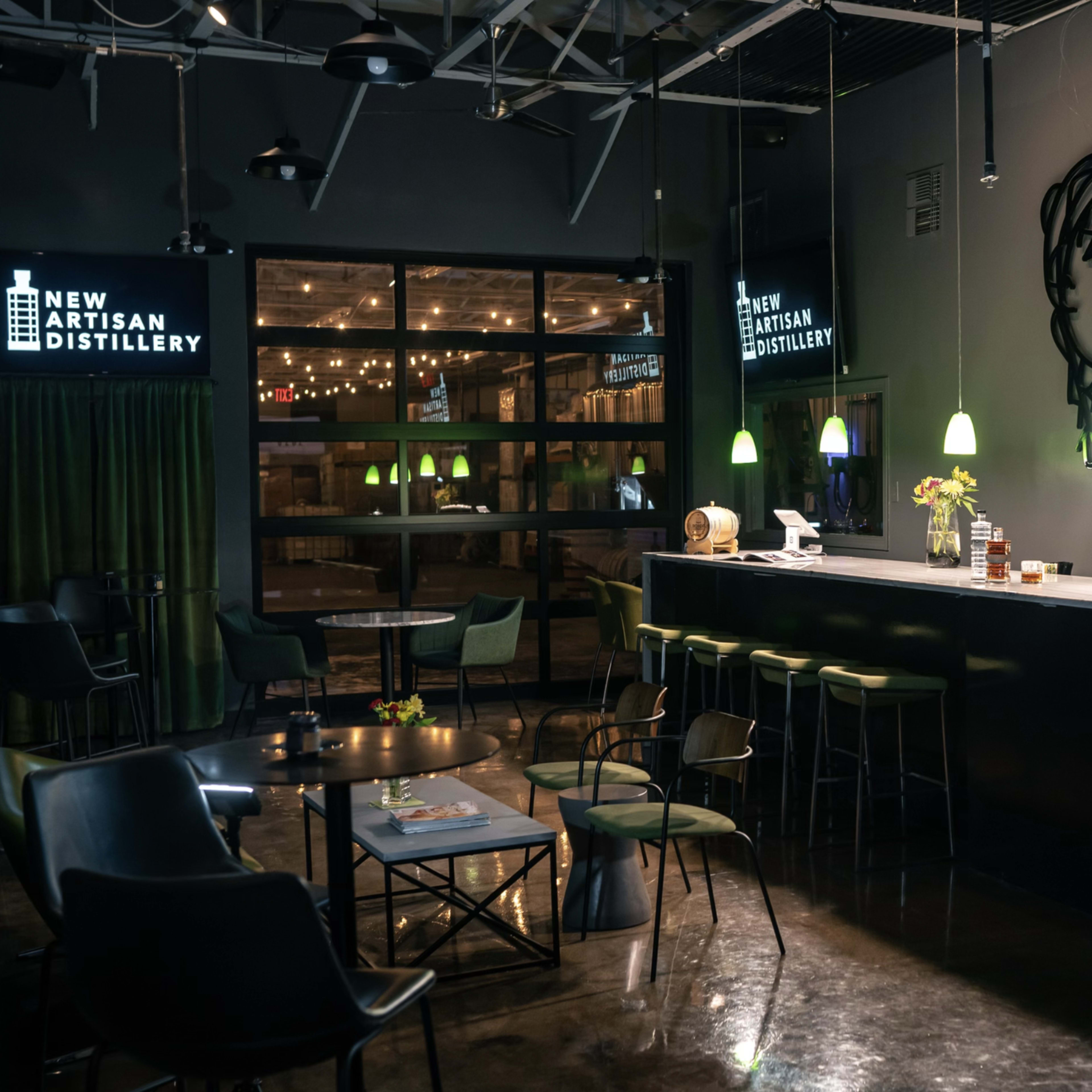A dimly lit distillery interior featuring a long bar with modern stools and tables under illuminated signs.