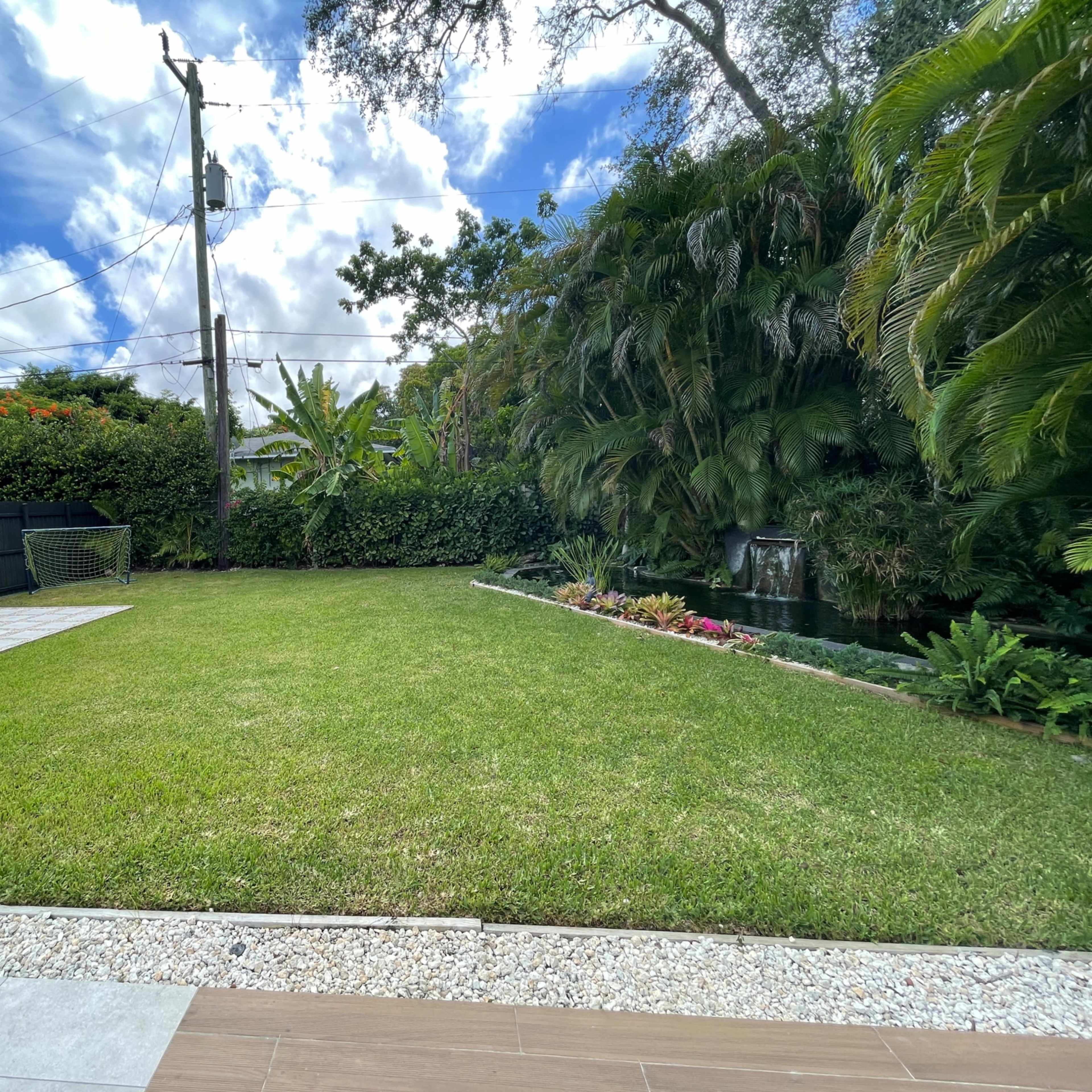 A well-maintained backyard with a grassy area, bordered by lush greenery and a stone pathway.