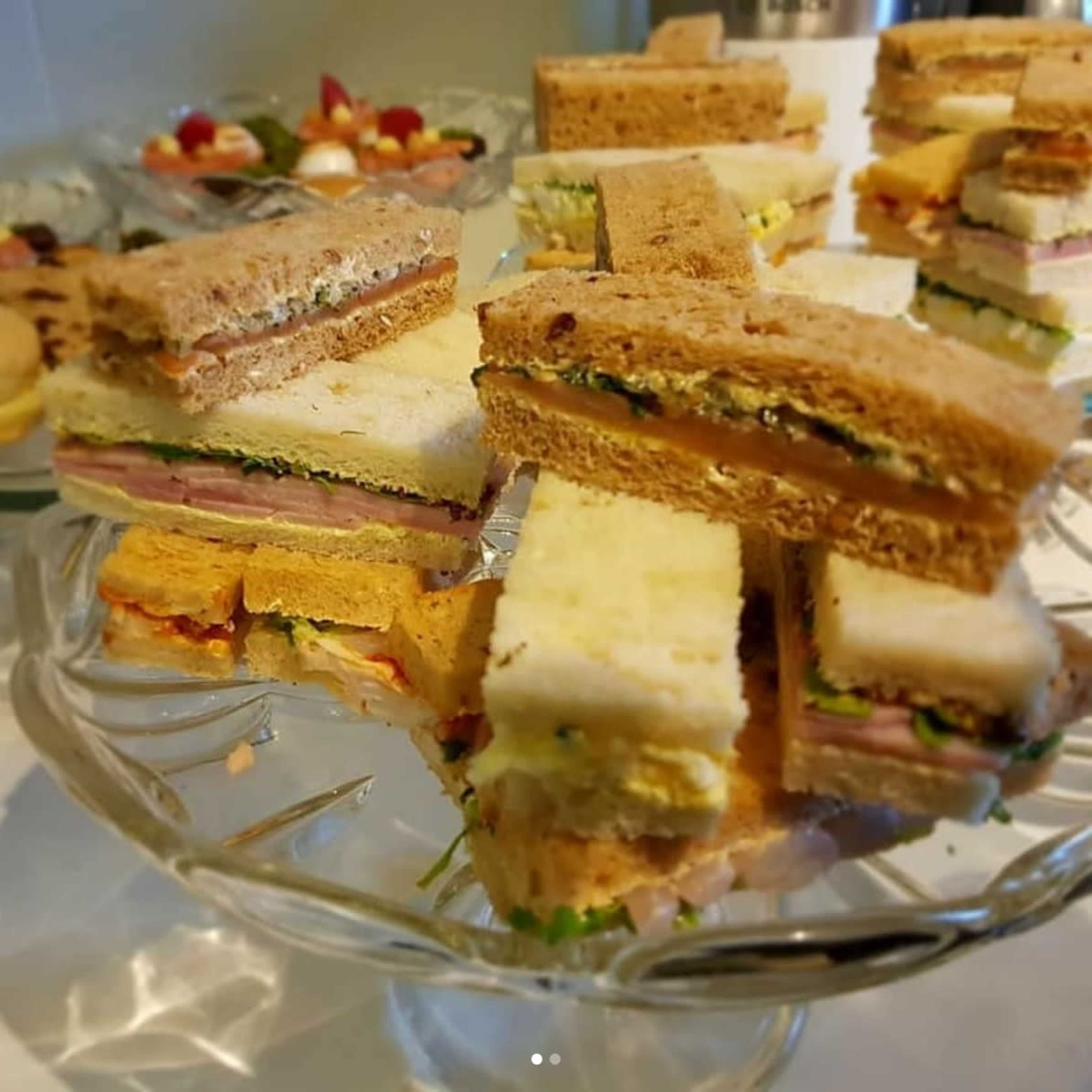 A glass platter holds an assortment of stacked sandwiches made with various fillings and whole-grain bread.