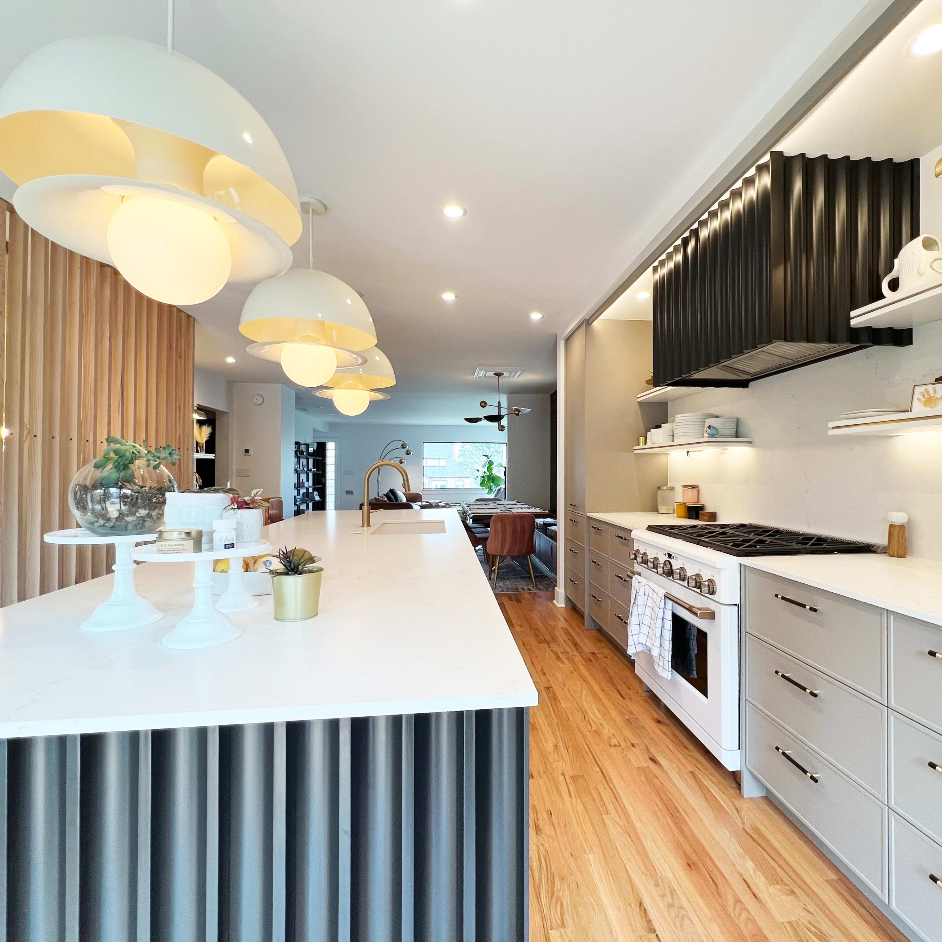 The kitchen features a long white island with ribbed black cabinetry, modern pendant lights, and stainless steel appliances.
