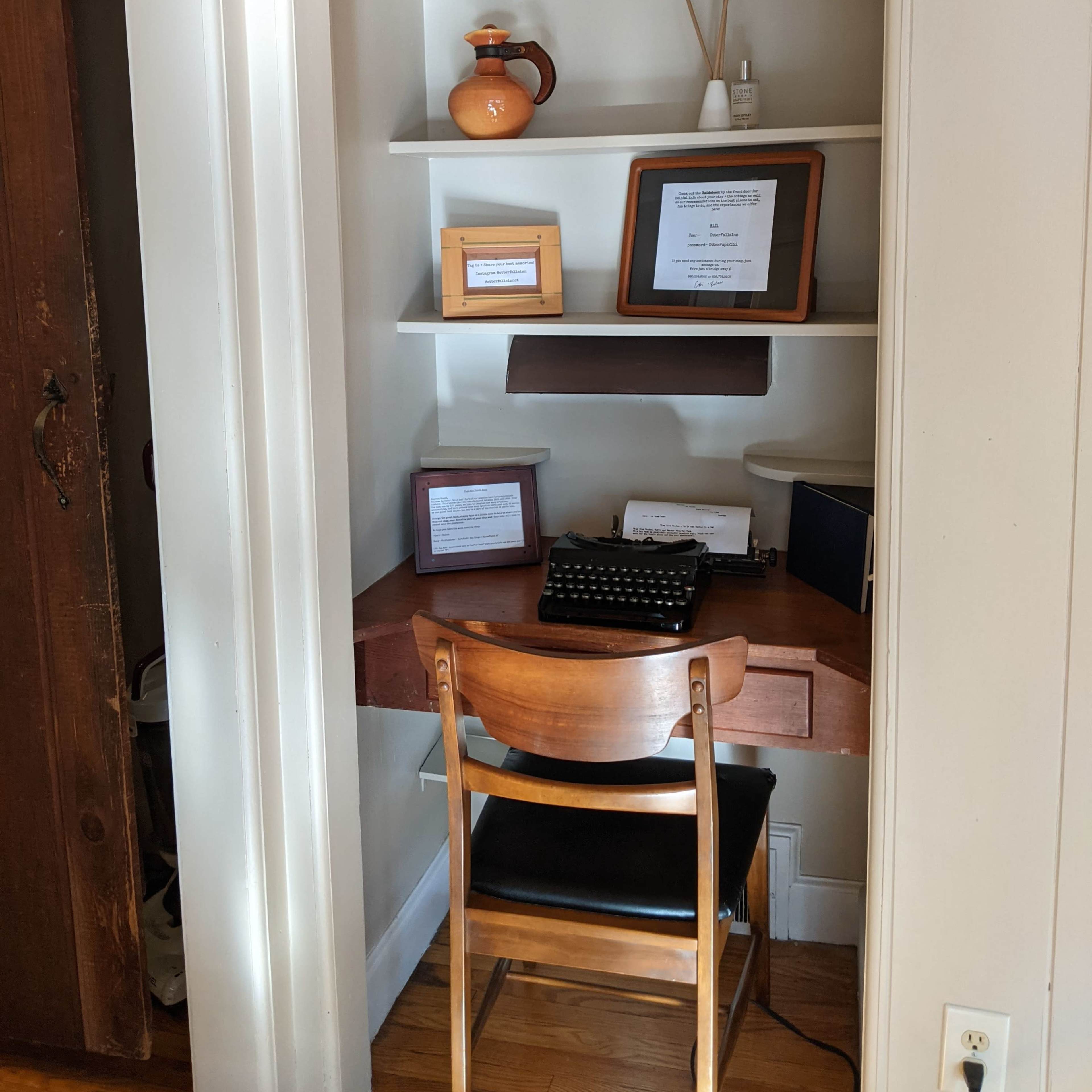 A small nook with shelves displaying decorative items and a wooden desk with a typewriter and framed documents.