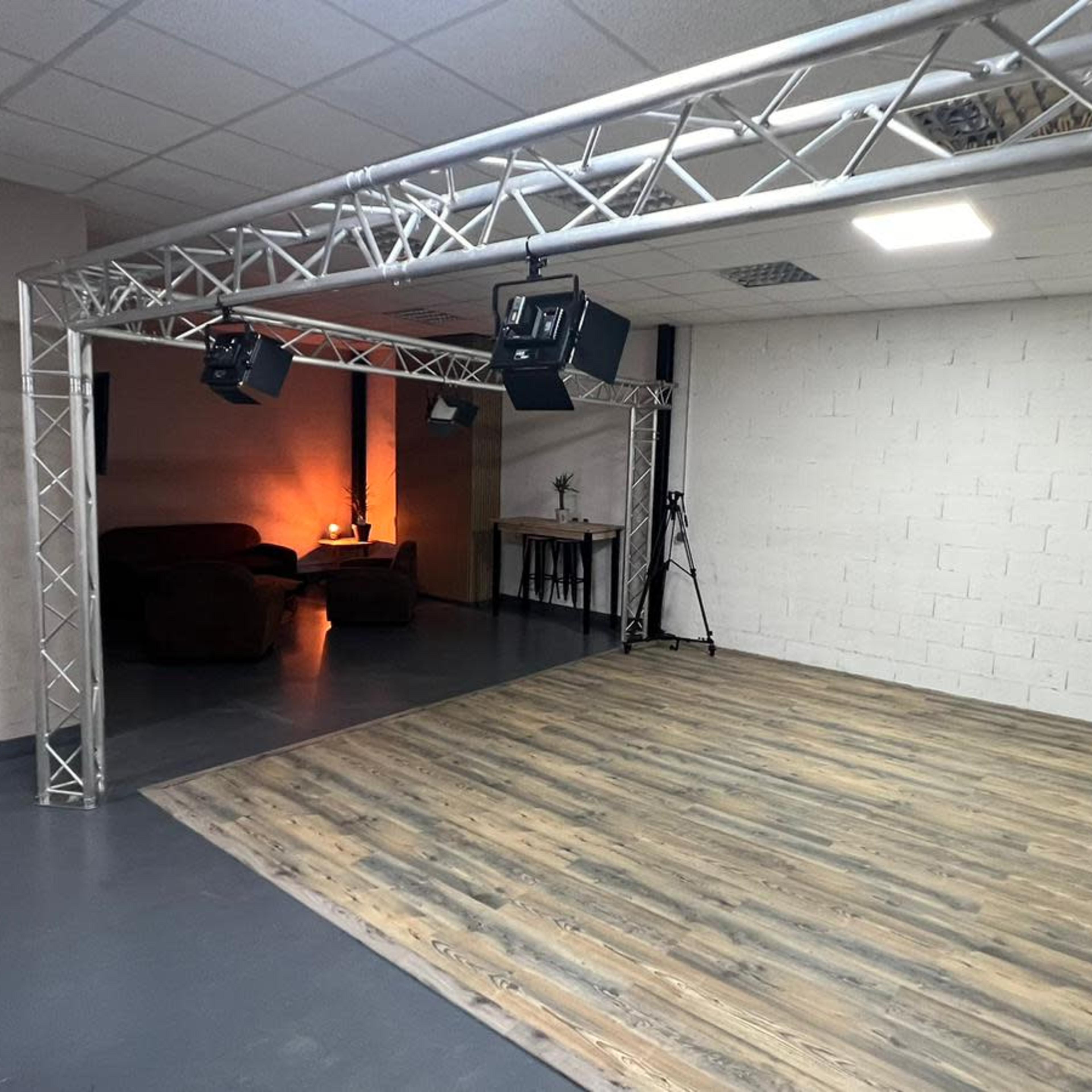 An empty room with wooden flooring, a wall-mounted clock, and lighting equipment set up for a studio or performance space.