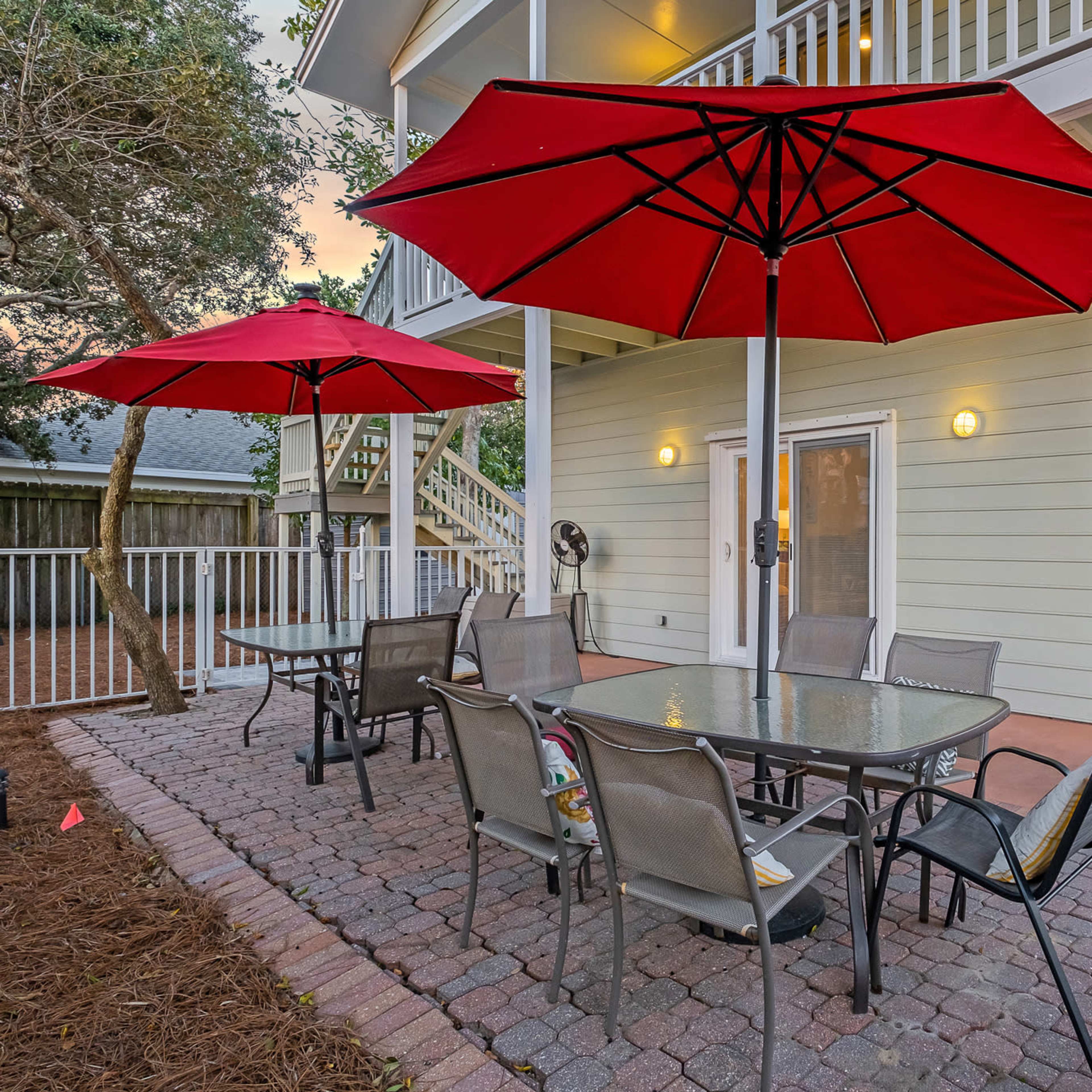 A patio area with two large red umbrellas covering metal tables and chairs near a light-colored building with stairs.