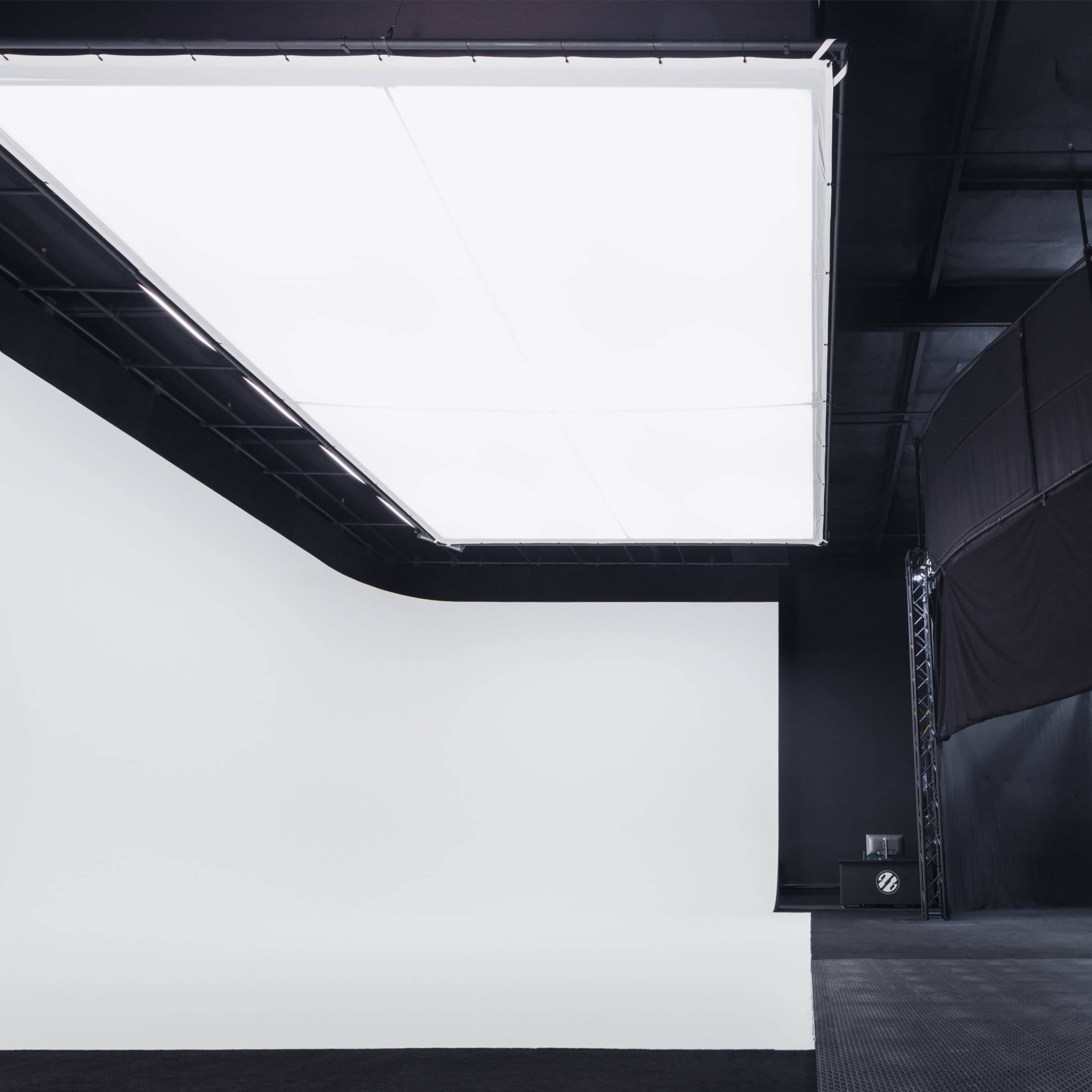 A spacious studio with a large white backdrop on one side and a circular platform enclosed by black fabric on the other.
