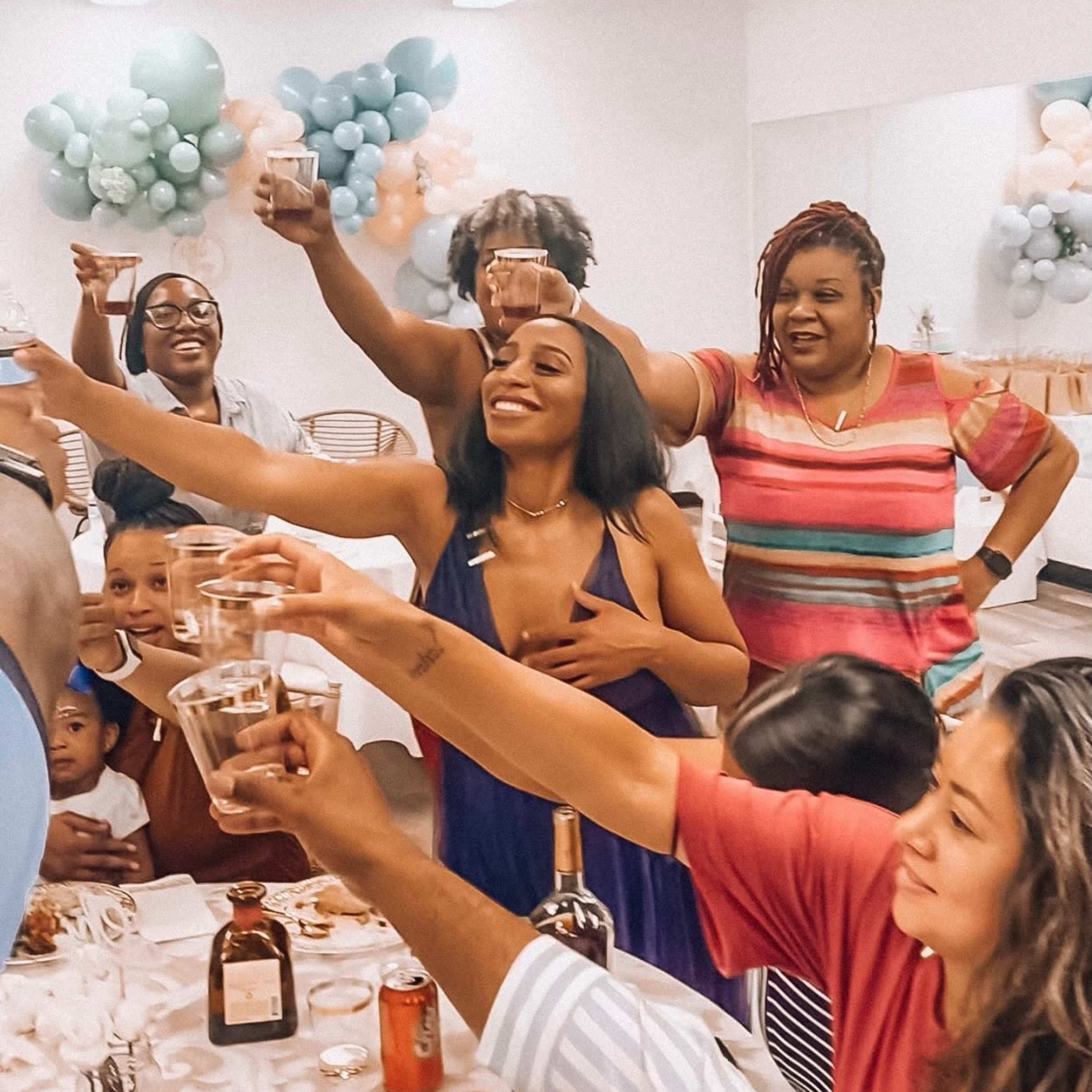 A group of people gather around a table in a festive setting, raising glasses in celebration.