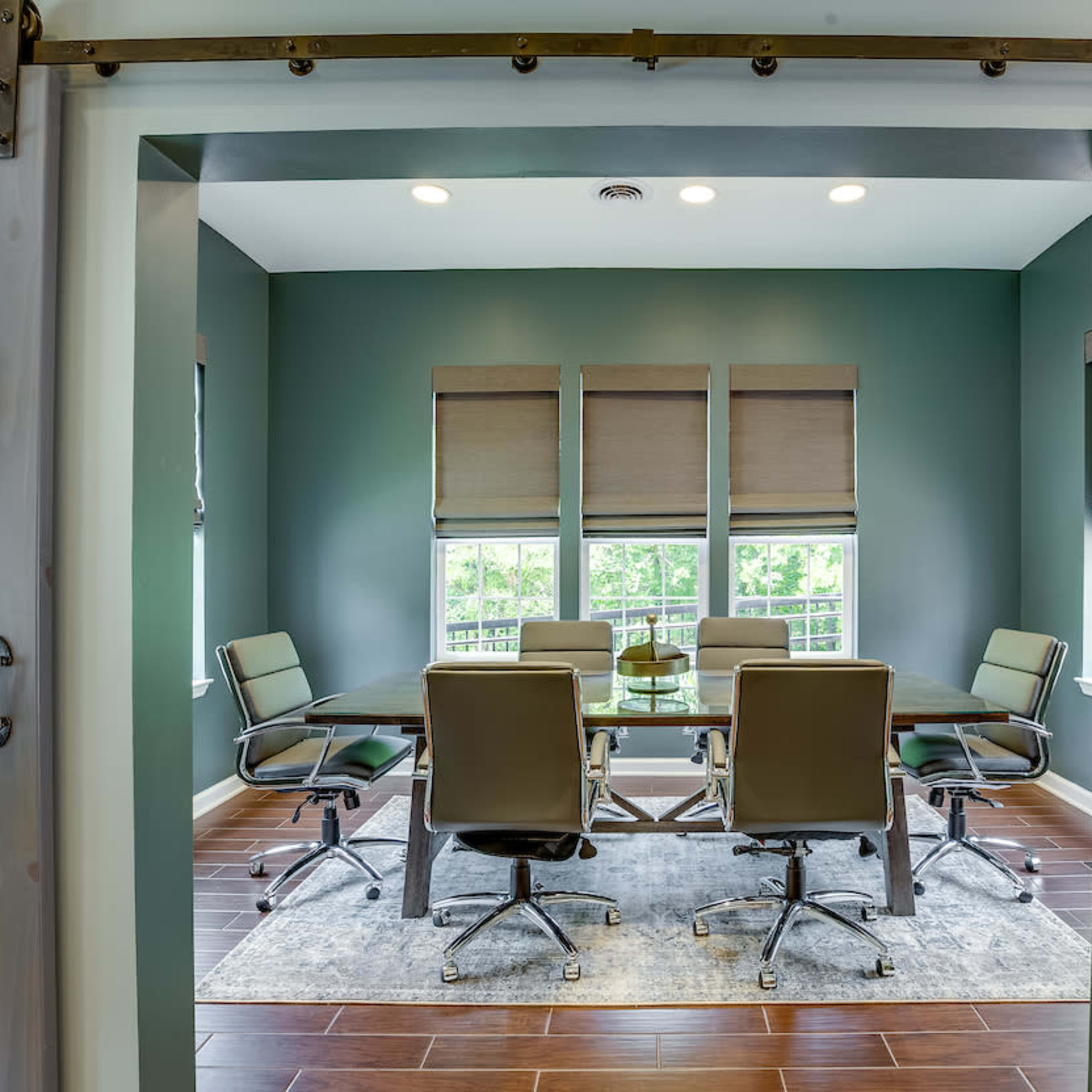 A modern conference room features a table surrounded by six ergonomic chairs, with large windows allowing natural light to brighten the space.
