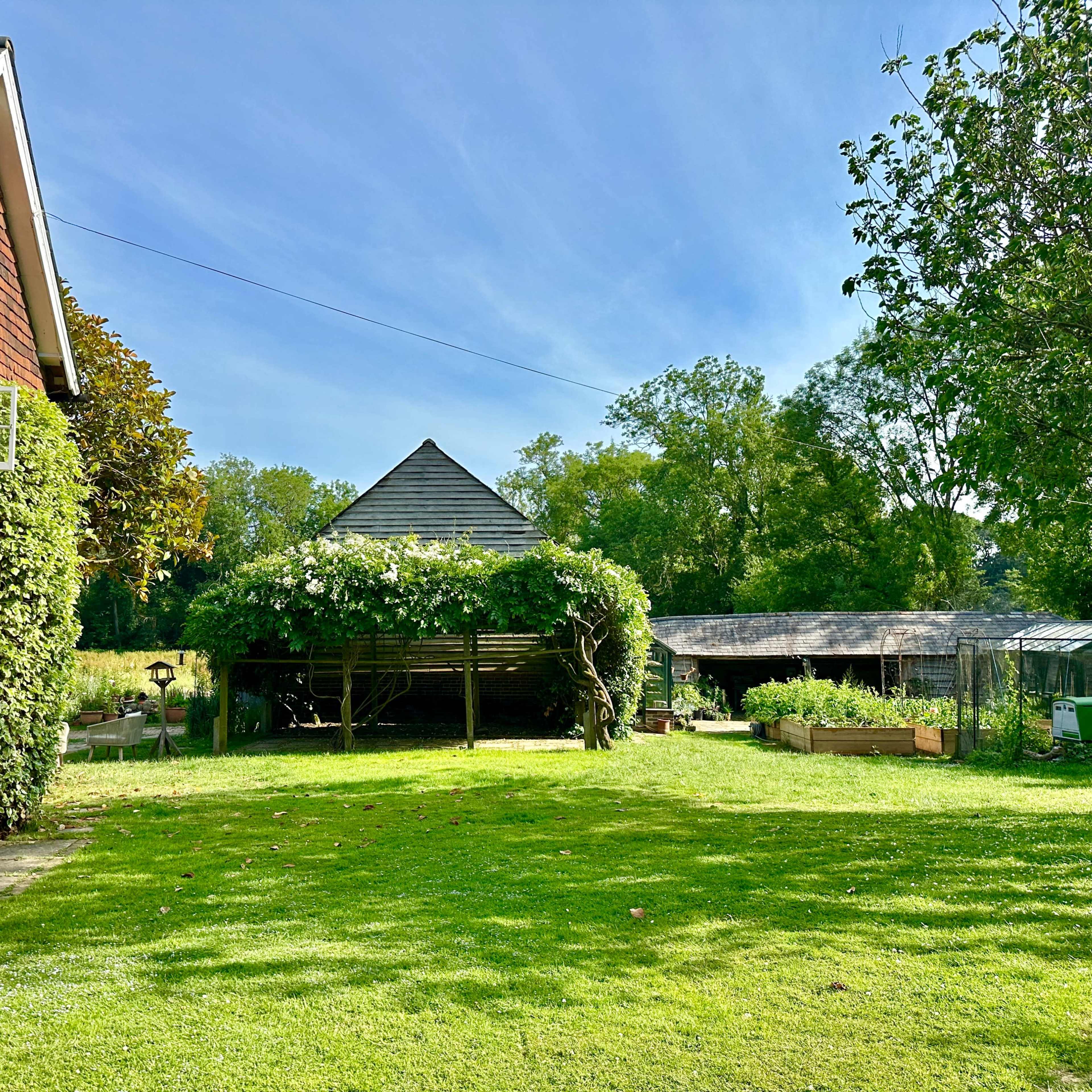 A garden with a brick house, a wooden shed, and a lush green lawn surrounded by trees.