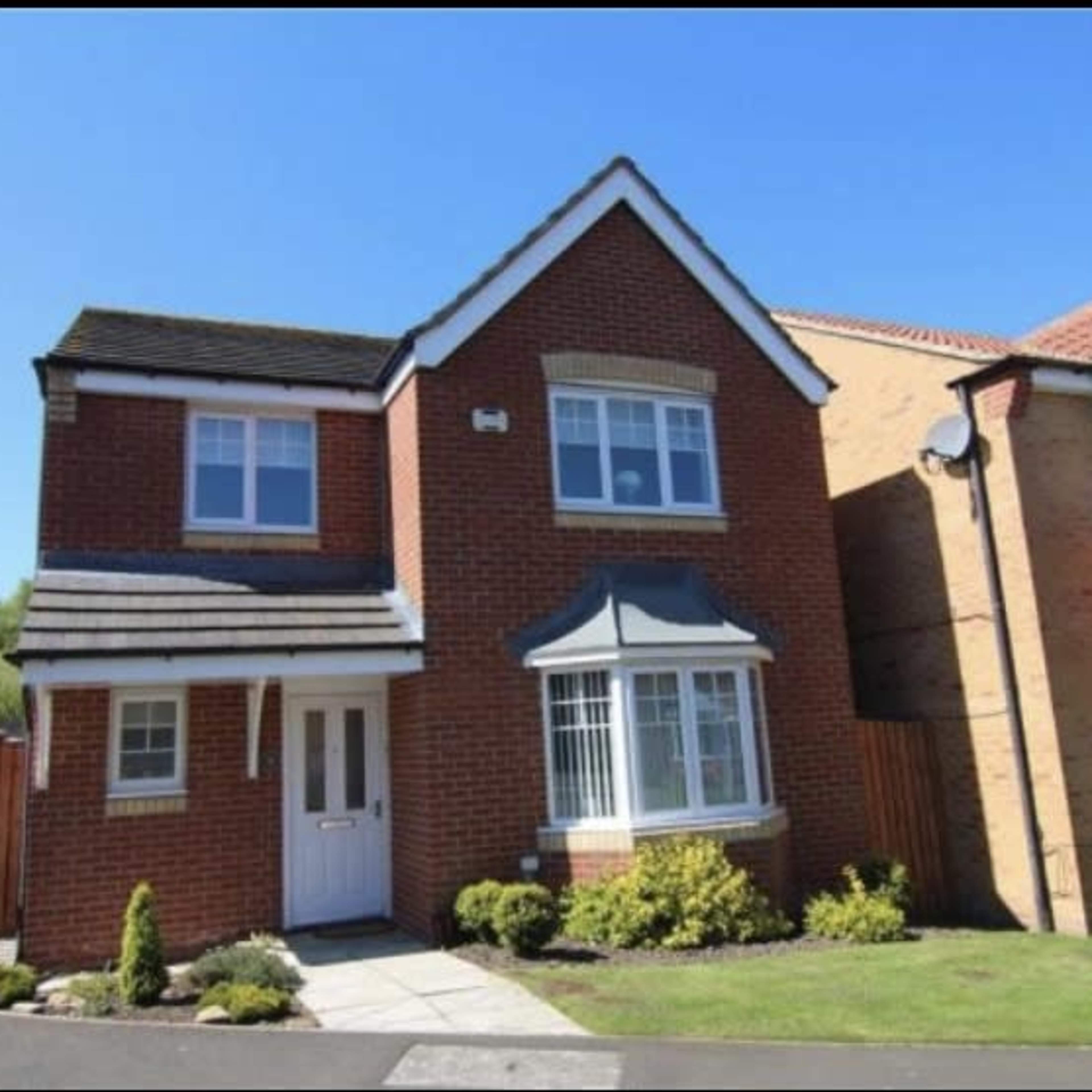 A two-story brick house with a sloped roof, a front porch, and landscaped garden is situated in a residential area.