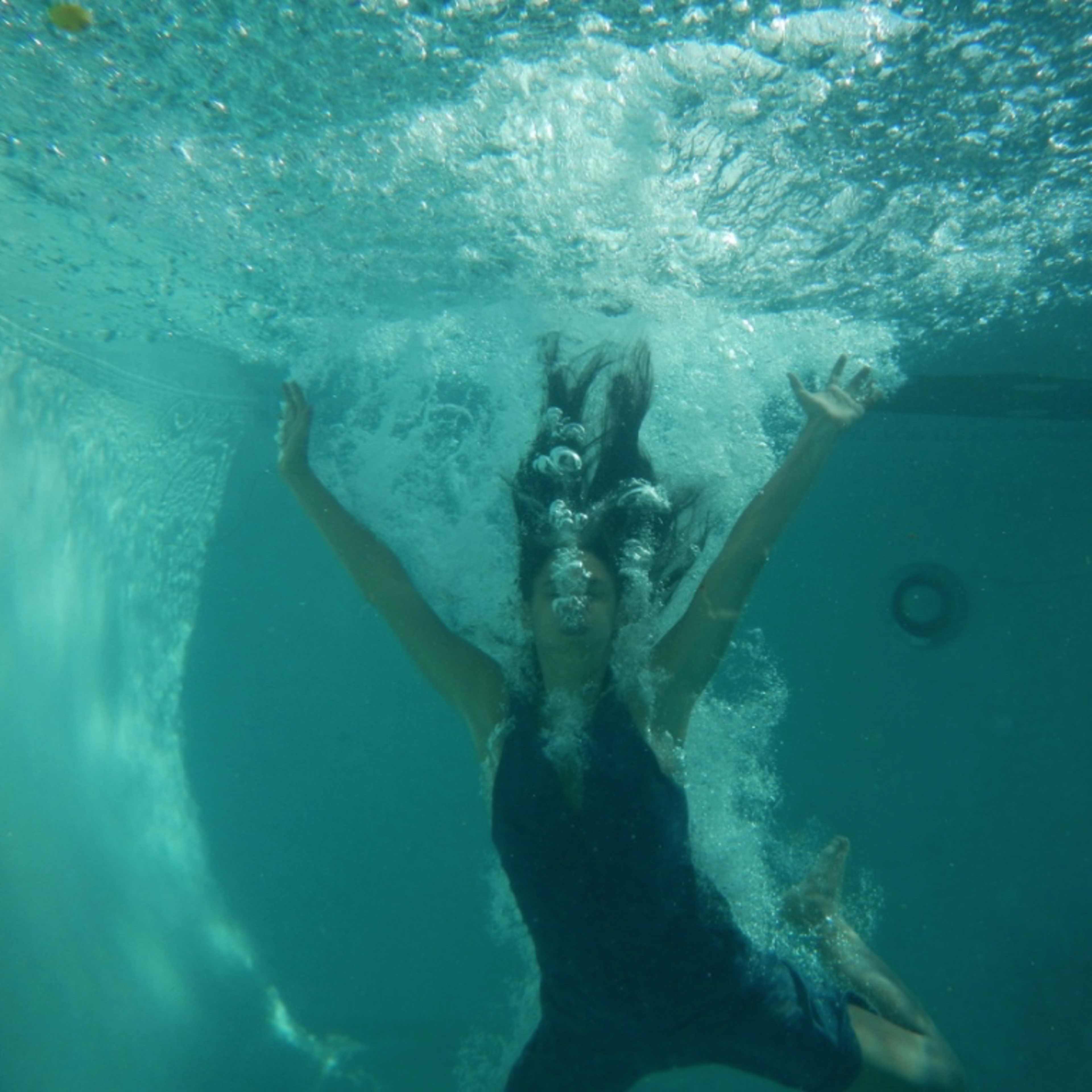 A person is submerged underwater, with bubbles surrounding them as they reach upward with both arms.