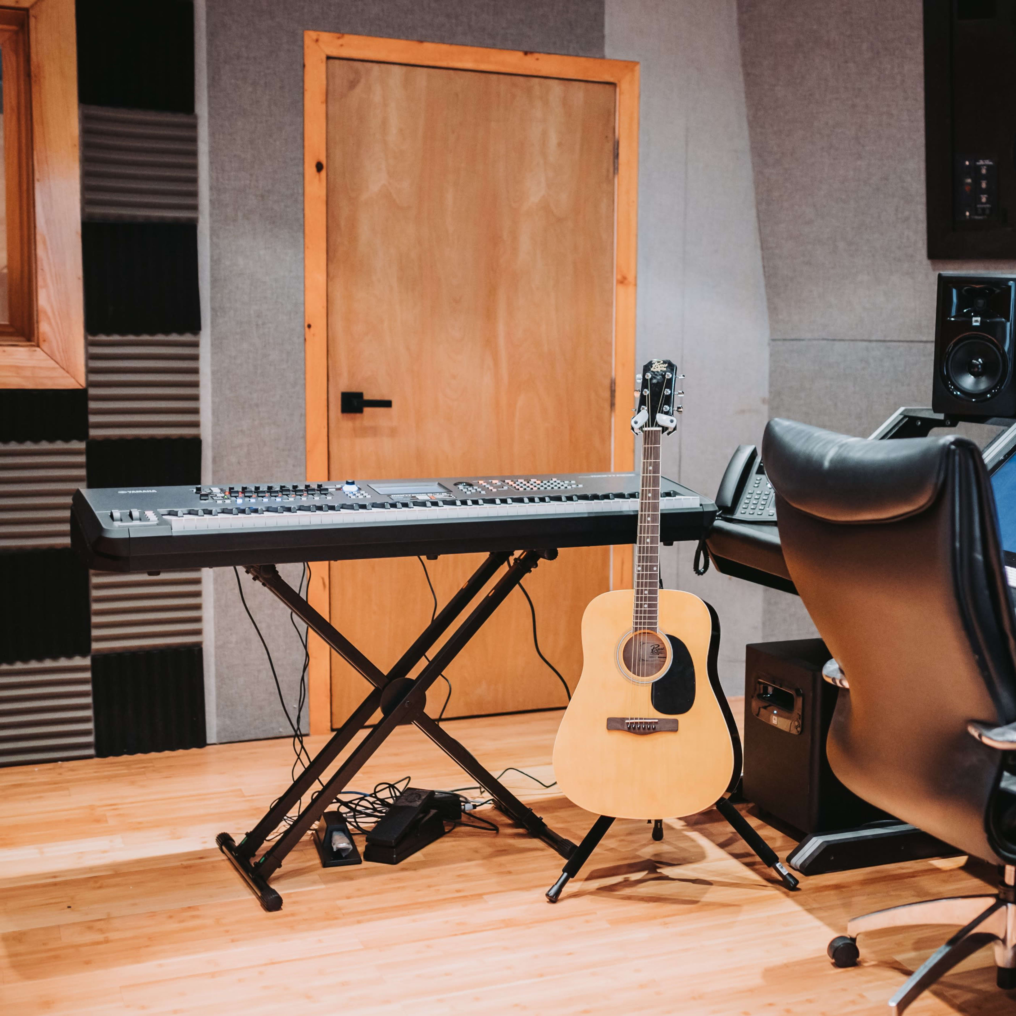A music studio featuring a keyboard, an acoustic guitar, and a sound mixing console surrounded by acoustic panels.