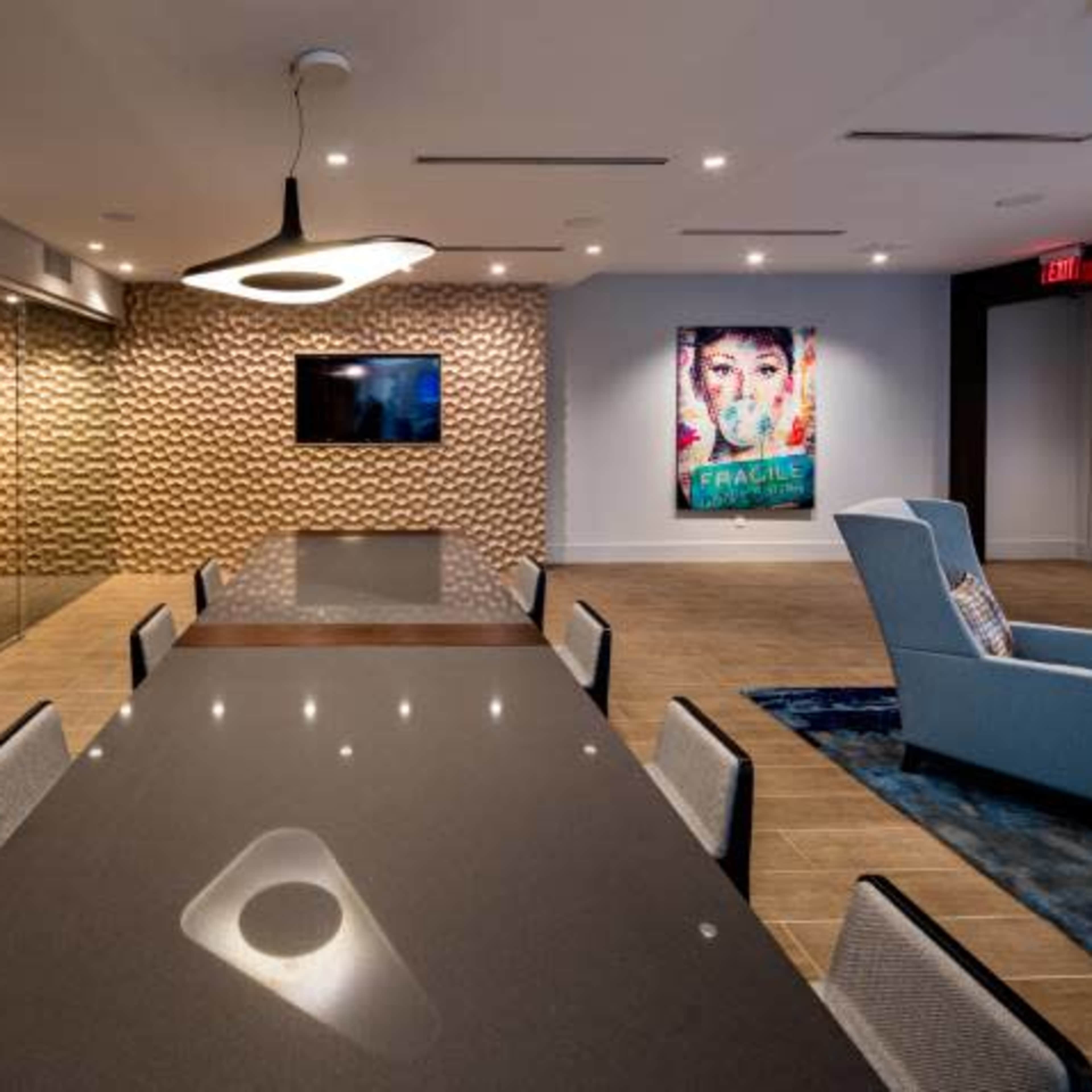A modern conference room features a long dark table, a large TV, and decorative wall art, illuminated by stylish overhead lighting.