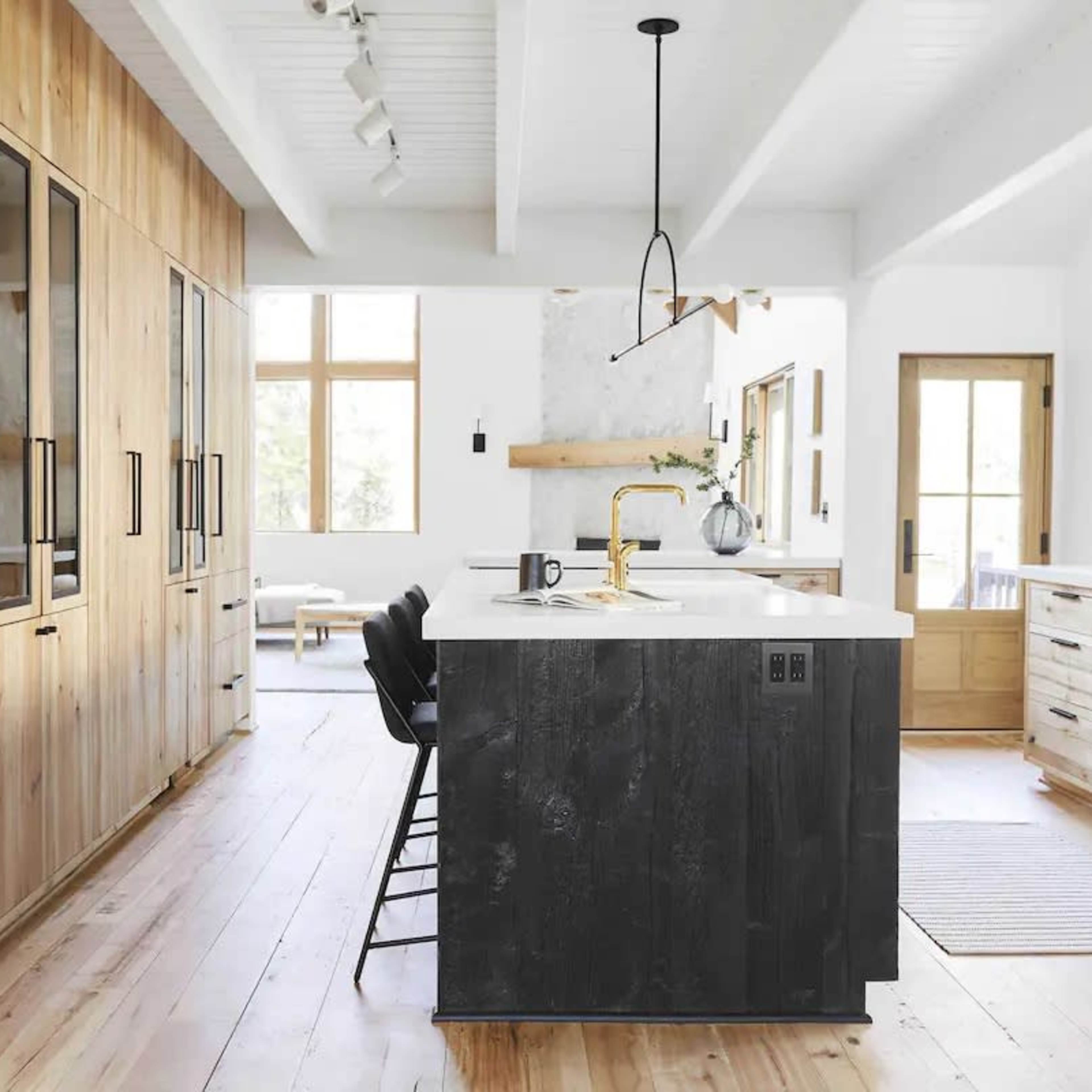 A modern kitchen features wooden cabinetry, a large island with a dark finish, and ample natural light from large windows.