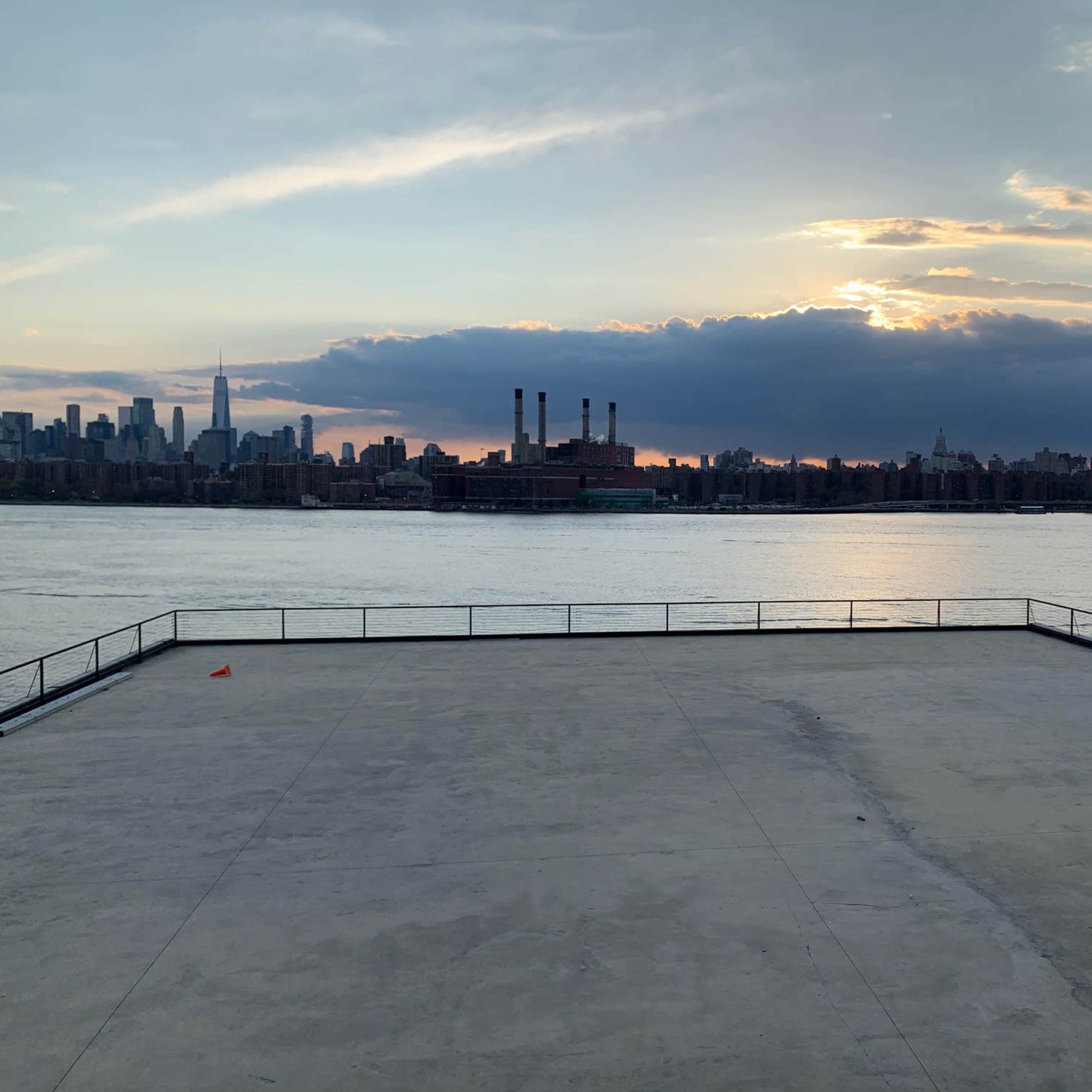A waterfront view of a city skyline at sunset with a clear expanse of water in the foreground.