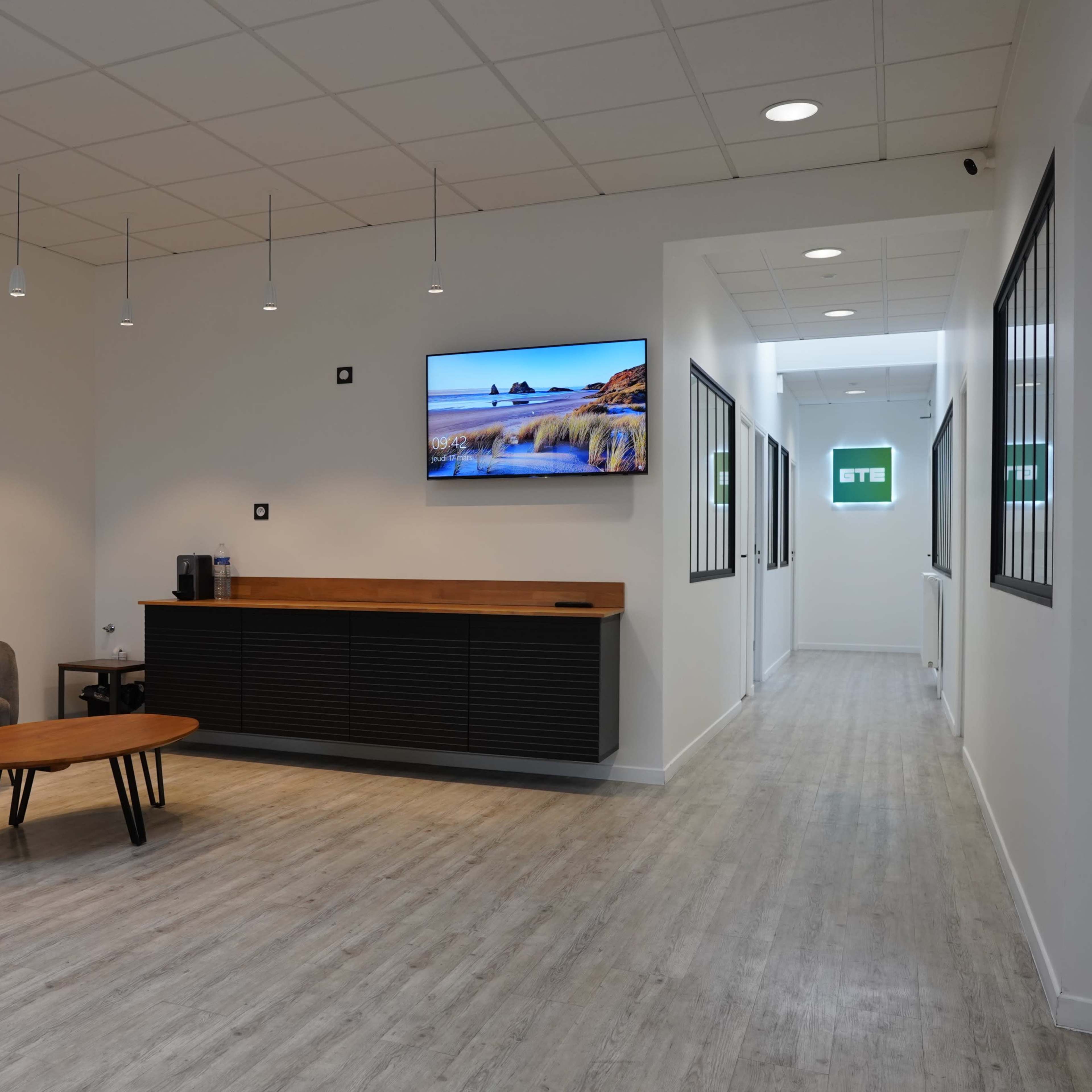 A contemporary office reception area featuring a green sofa, a wooden coffee table, and a wall-mounted television.