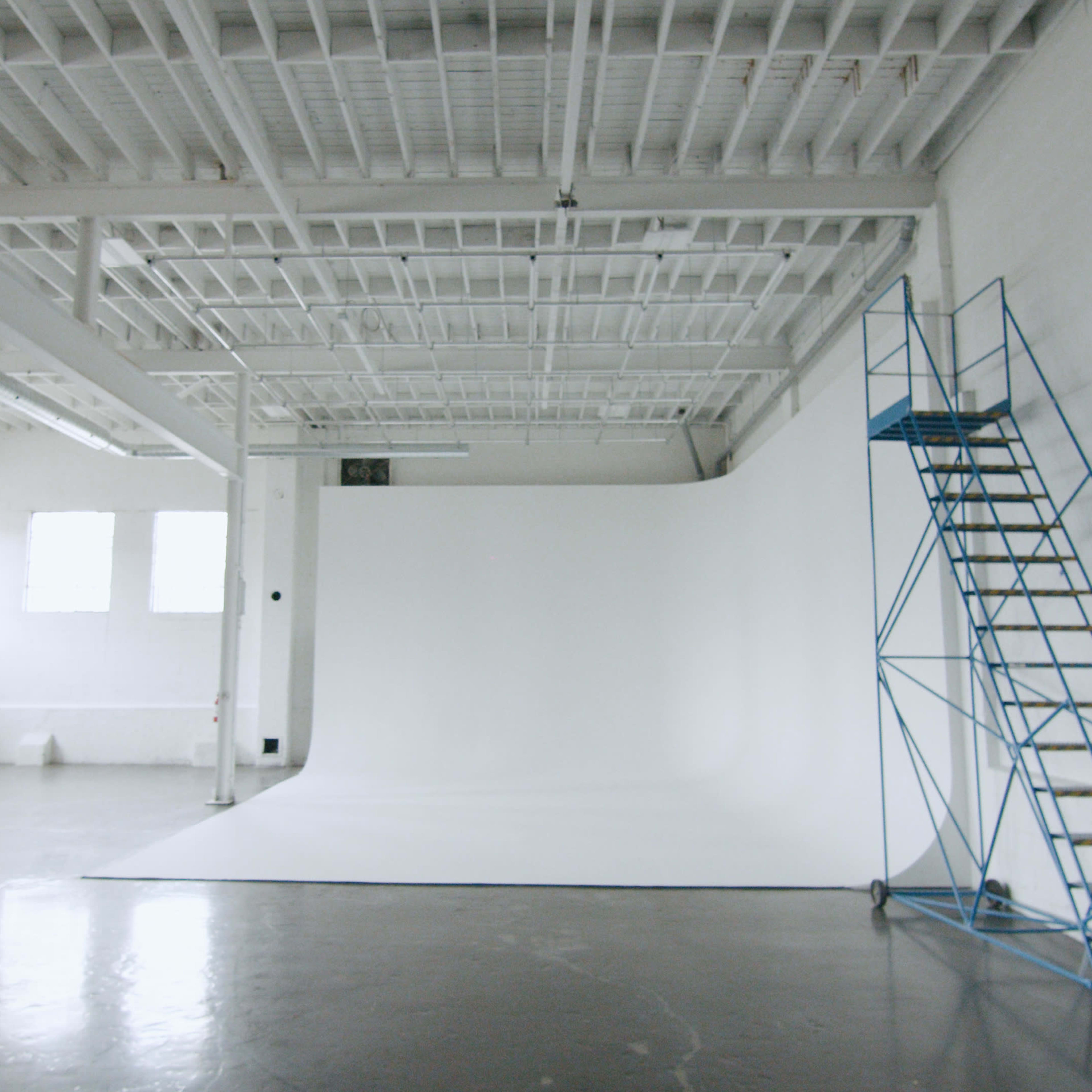 A spacious photography studio with a white seamless backdrop and a blue metal scaffolding on the side.