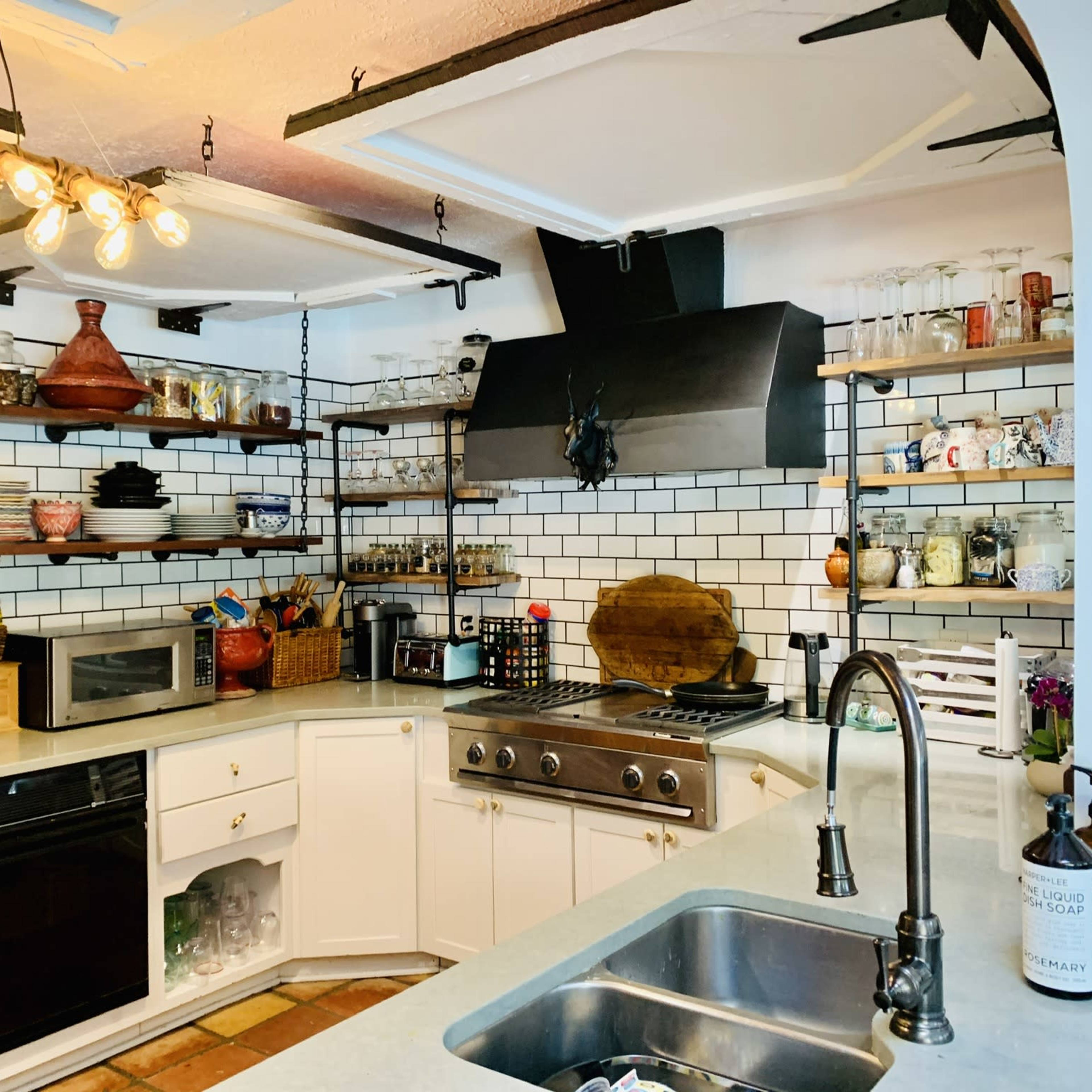 A modern kitchen with white cabinetry, open shelving displaying various dishware, a stainless steel stove, and a black exhaust hood.