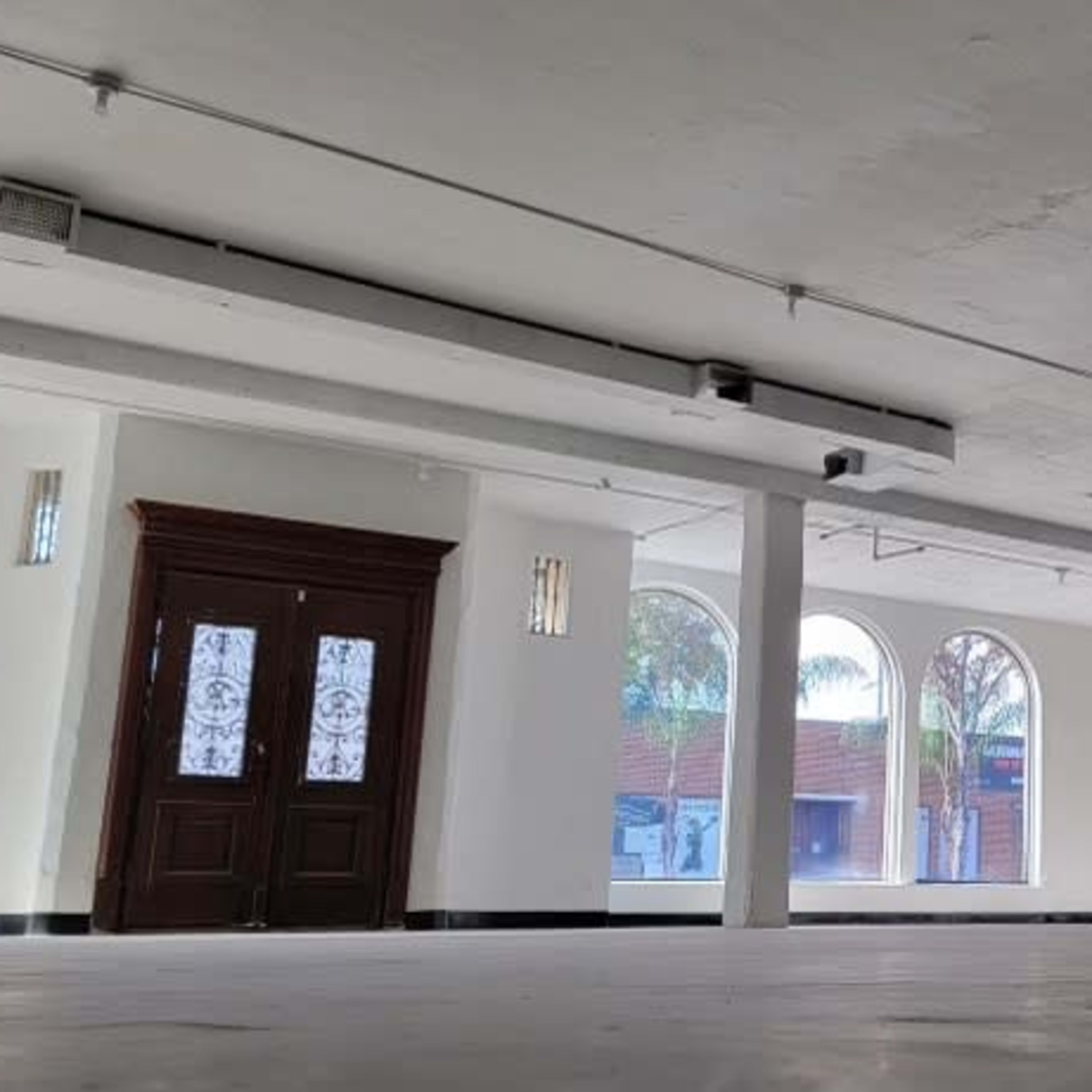 A spacious, empty interior room with large arched windows and a set of double doors.