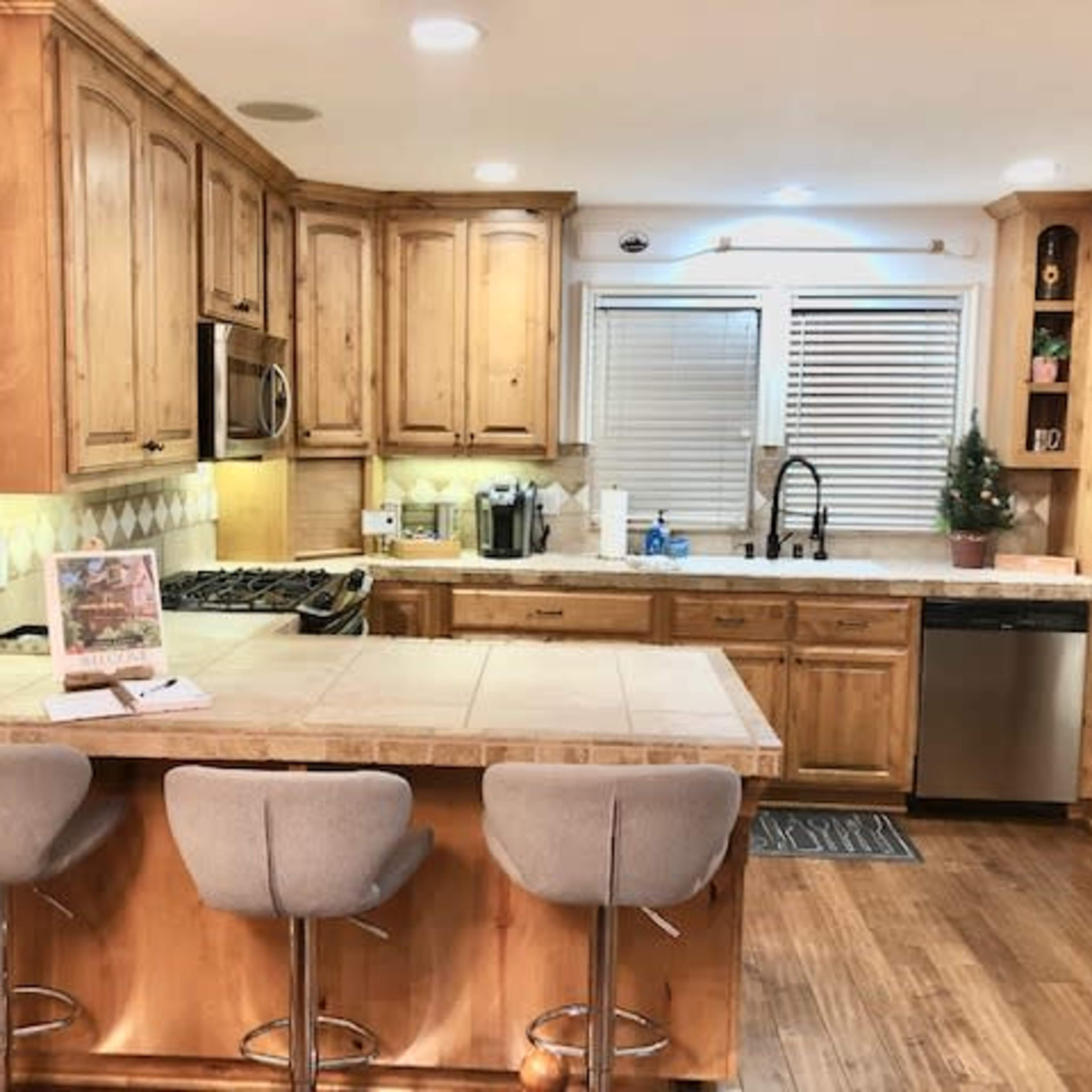 A kitchen features wooden cabinets, stainless steel appliances, a central island with bar stools, and a small decorative tree on the counter.