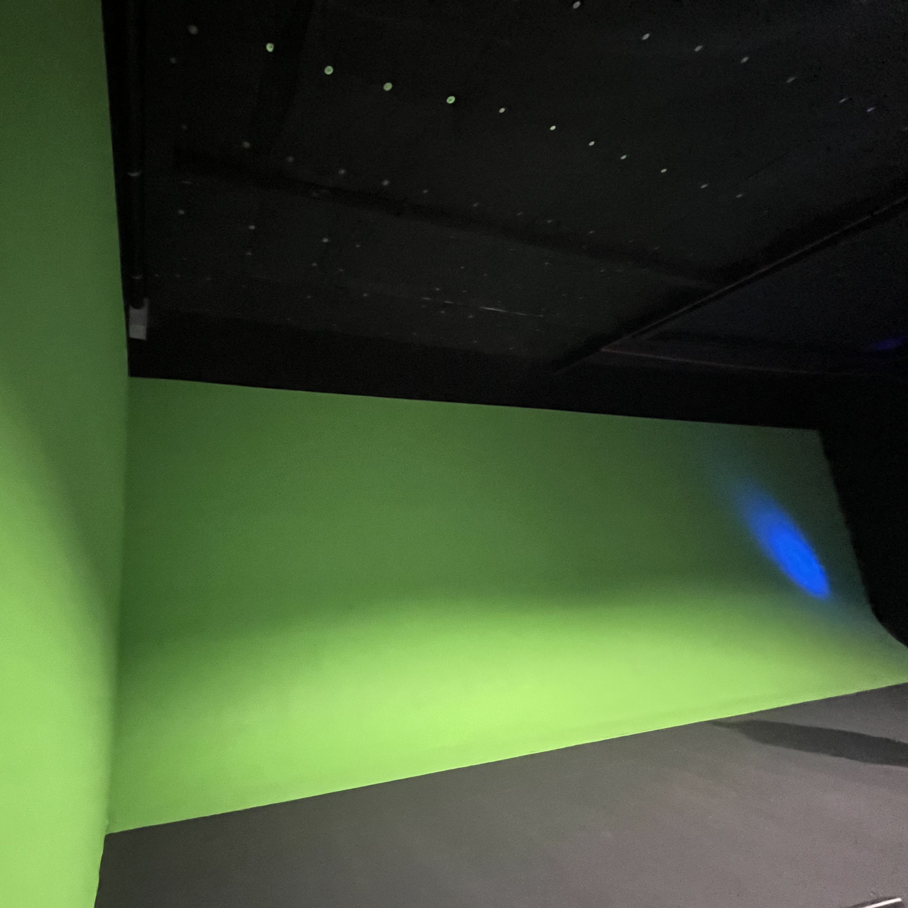 A room with two green walls and a black floor, likely set up for green screen filming.