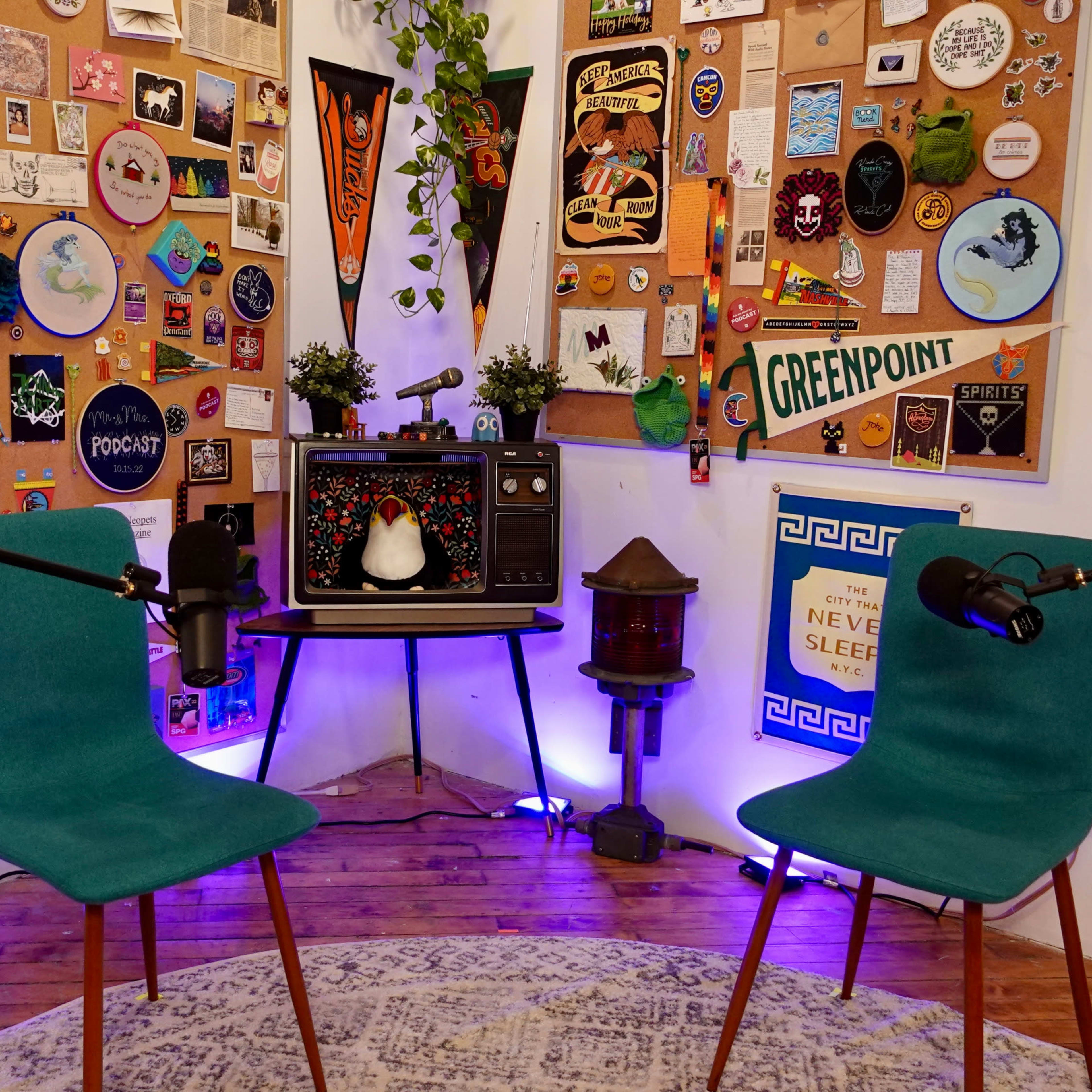 A cozy podcast or interview setup with two teal chairs facing a vintage-style display board adorned with various pins, posters, and decorations.