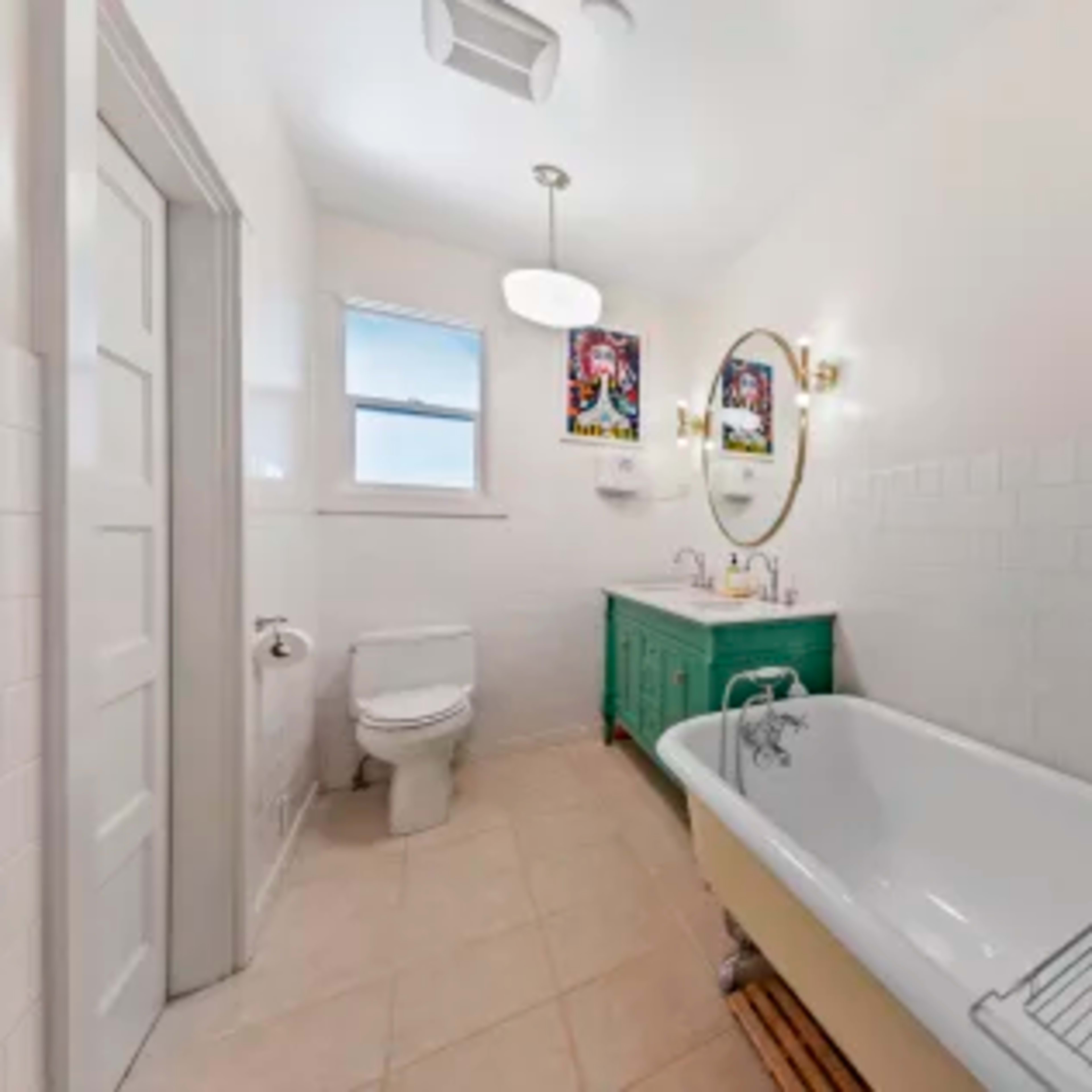 A bright bathroom featuring a white freestanding bathtub, a green vanity with sinks, and tiled walls.