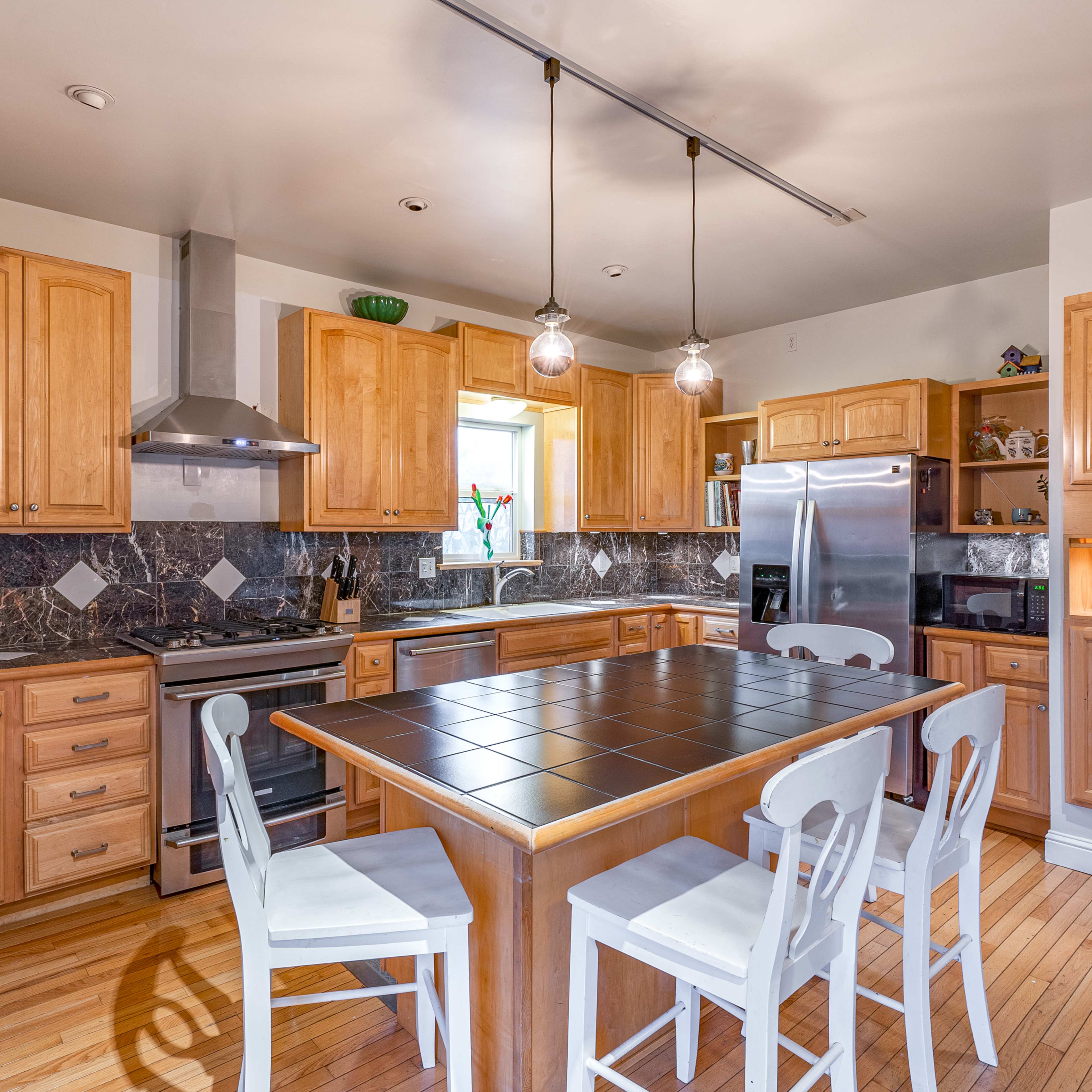 A modern kitchen features wooden cabinets, a central island with seating, stainless steel appliances, and a marble backsplash.