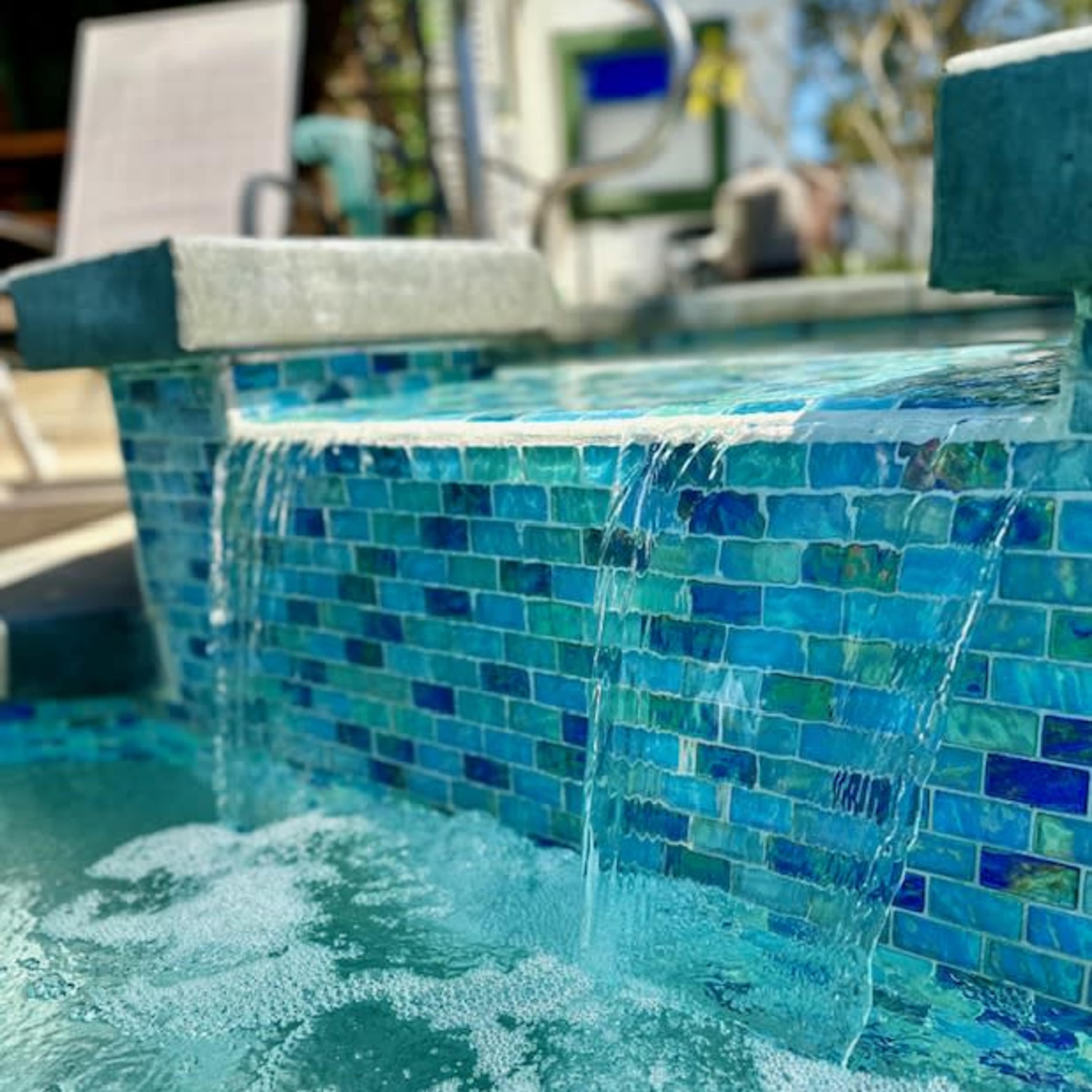 A small swimming pool features a mosaic-tiled wall with water cascading over the edge into the pool below.
