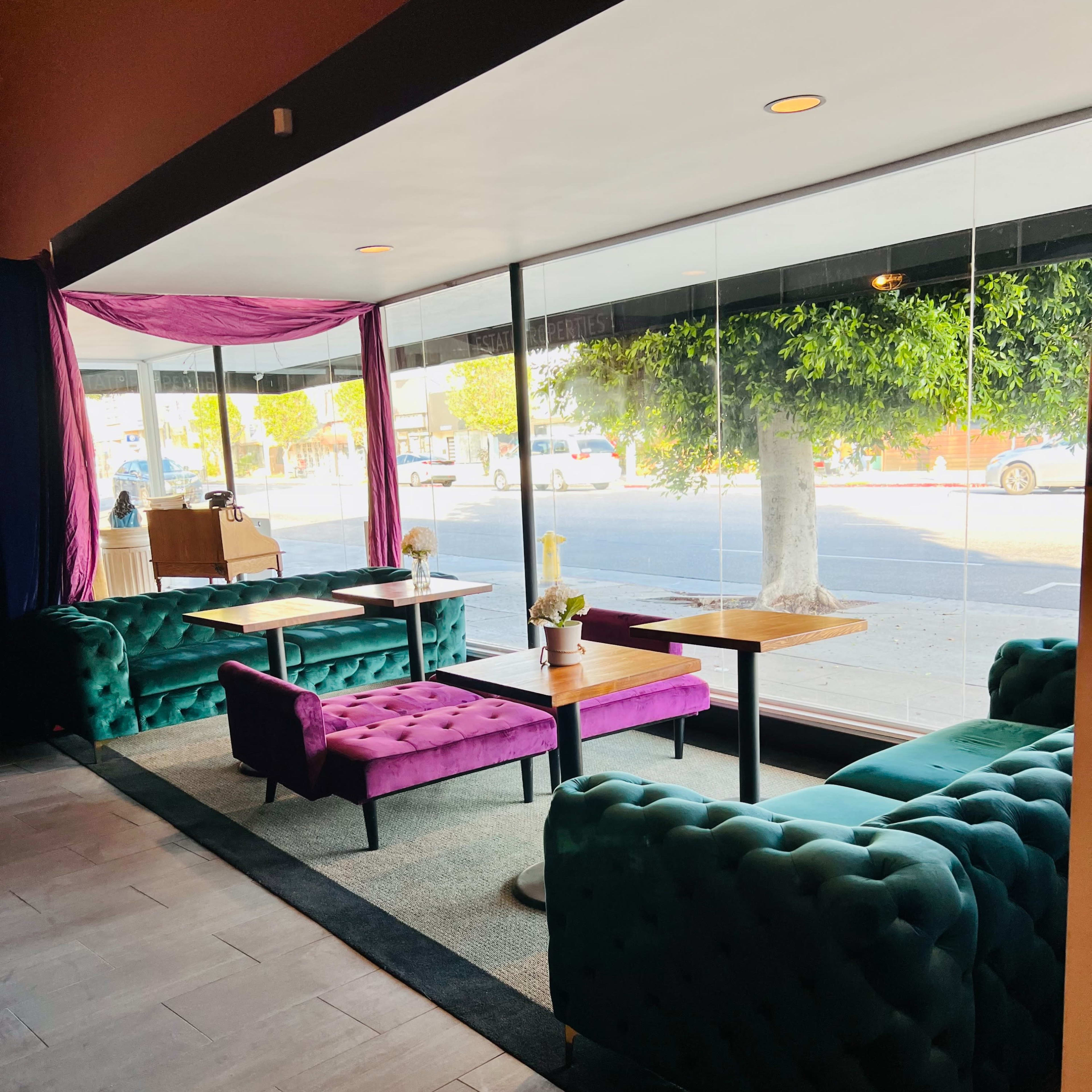 A modern seating area with green and purple tufted couches and tables, illuminated by natural light through large windows.