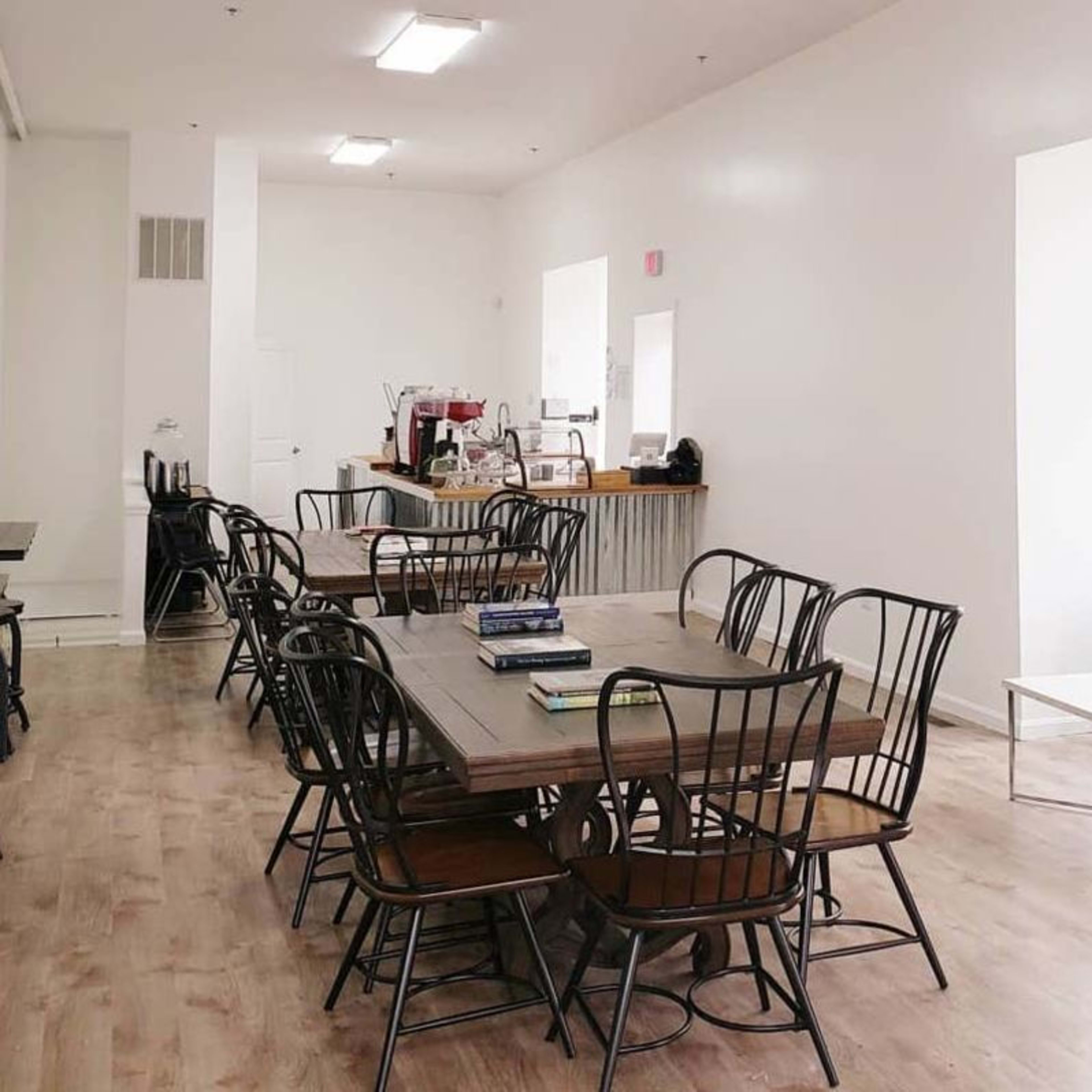 A bright, spacious café with wooden tables, black chairs, and a green couch along the wall.