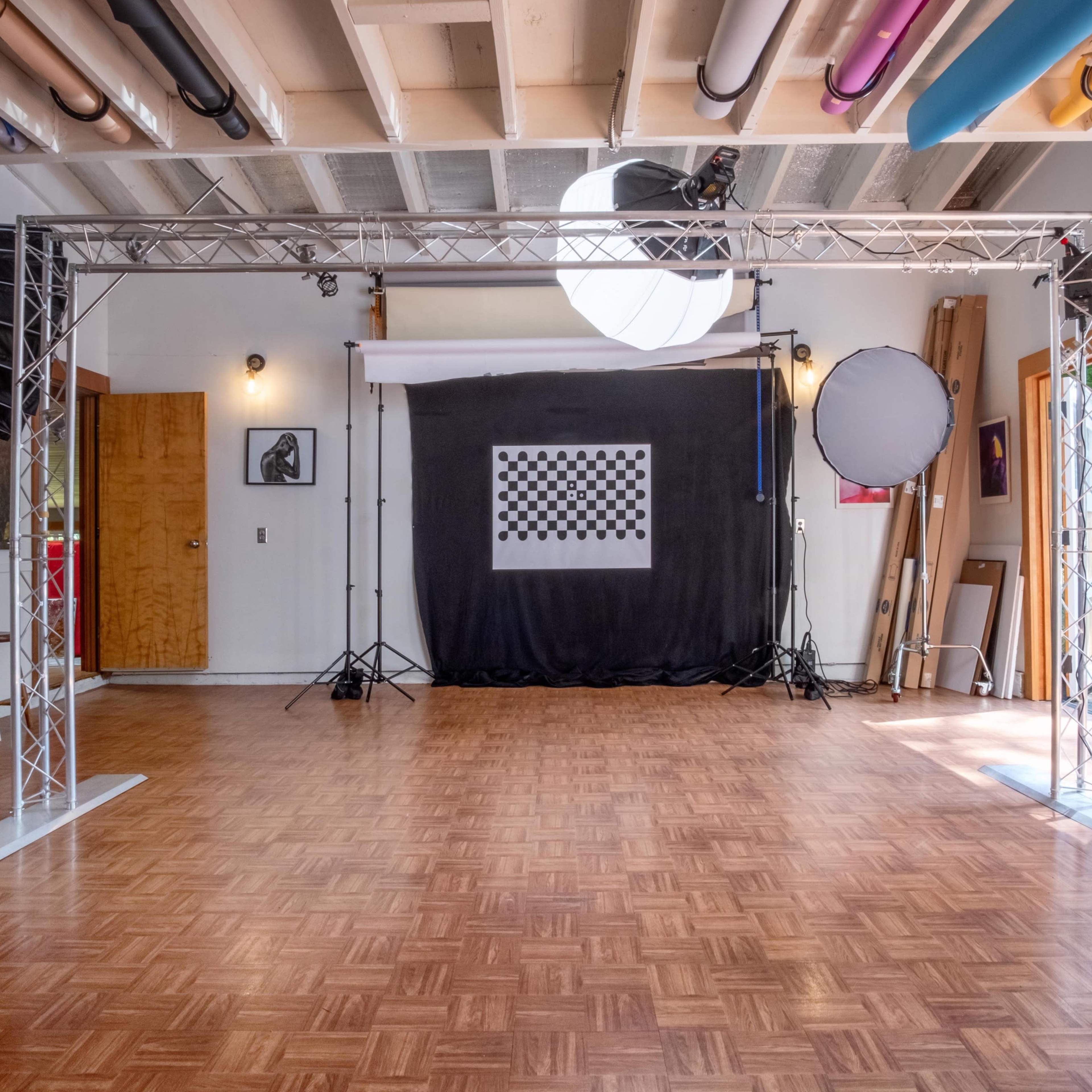 A photography studio setup featuring a checkerboard backdrop, lighting equipment, and a wooden floor.