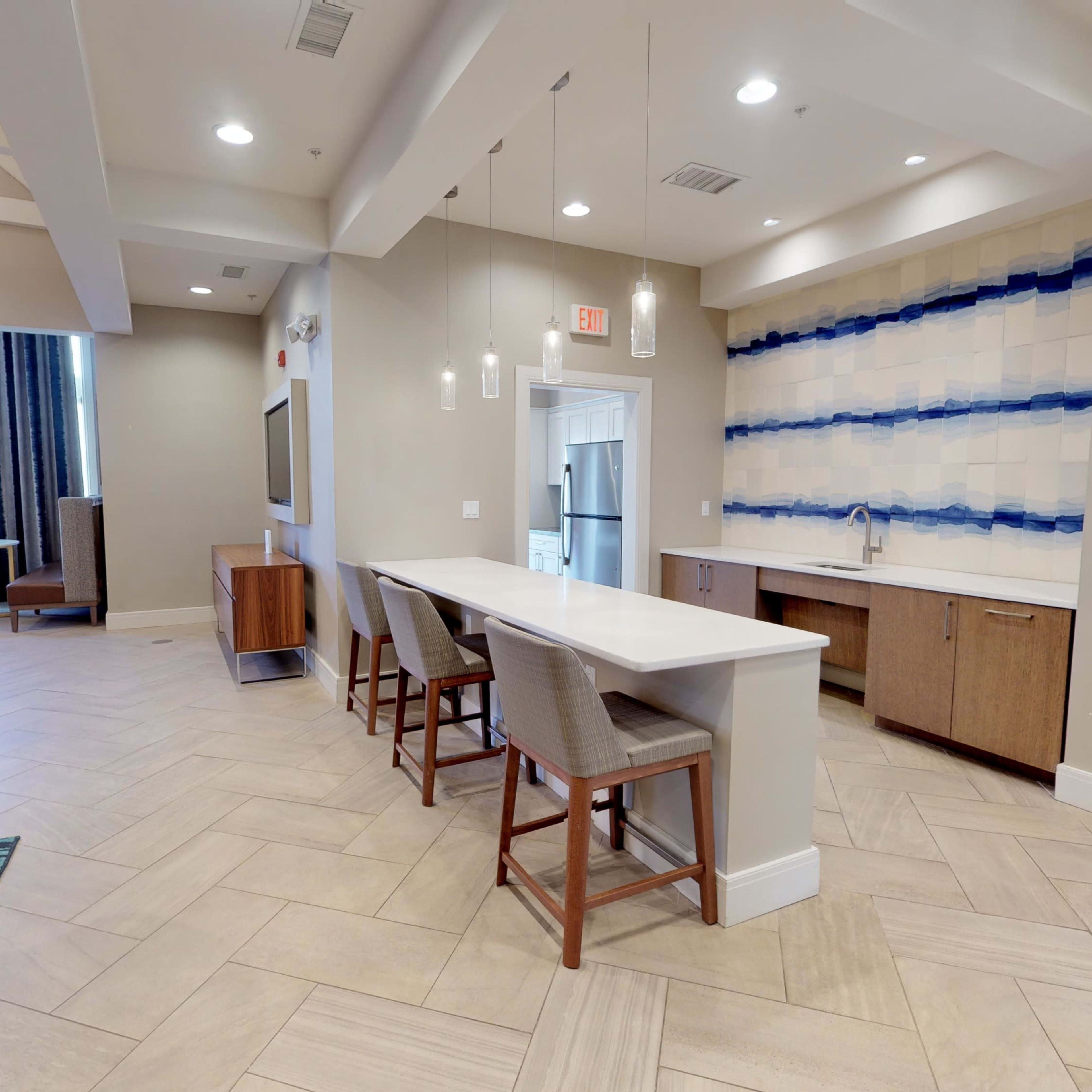A modern interior space featuring a seating area, a kitchen counter with stools, and decorative wall paneling.
