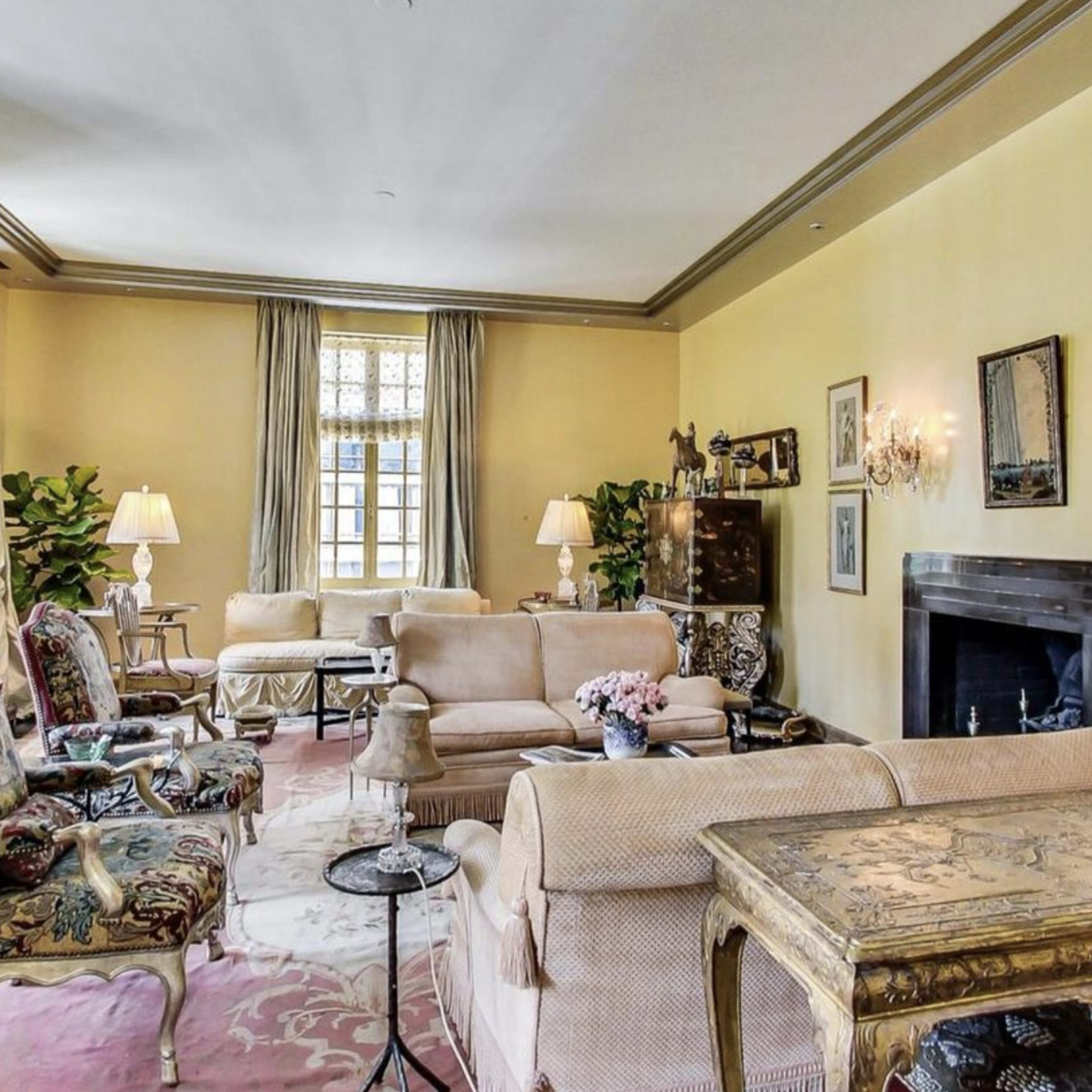 A living room with light yellow walls, a fireplace, and antique furniture arranged around a central area rug.