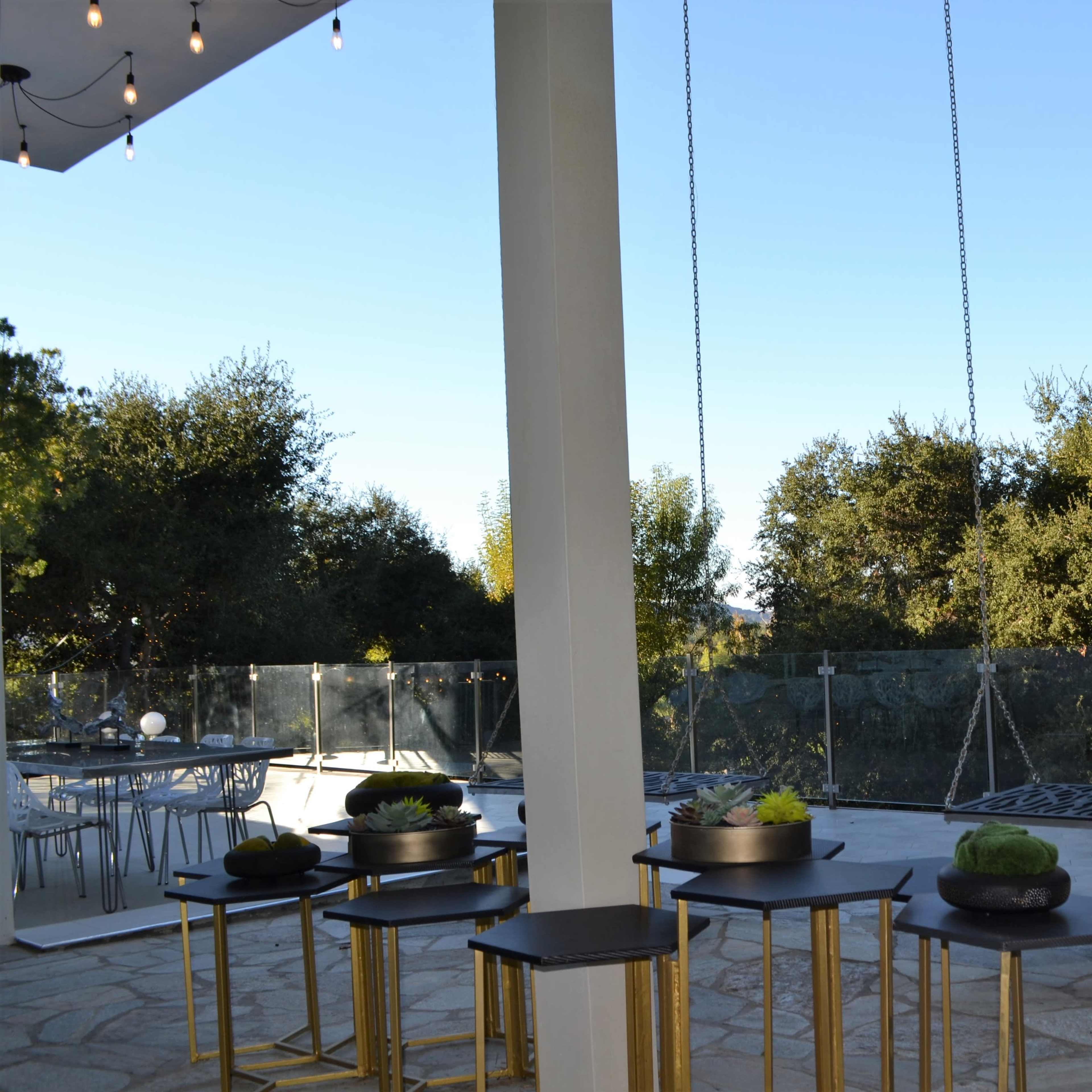 A modern patio area with hanging swings and small tables surrounded by trees.