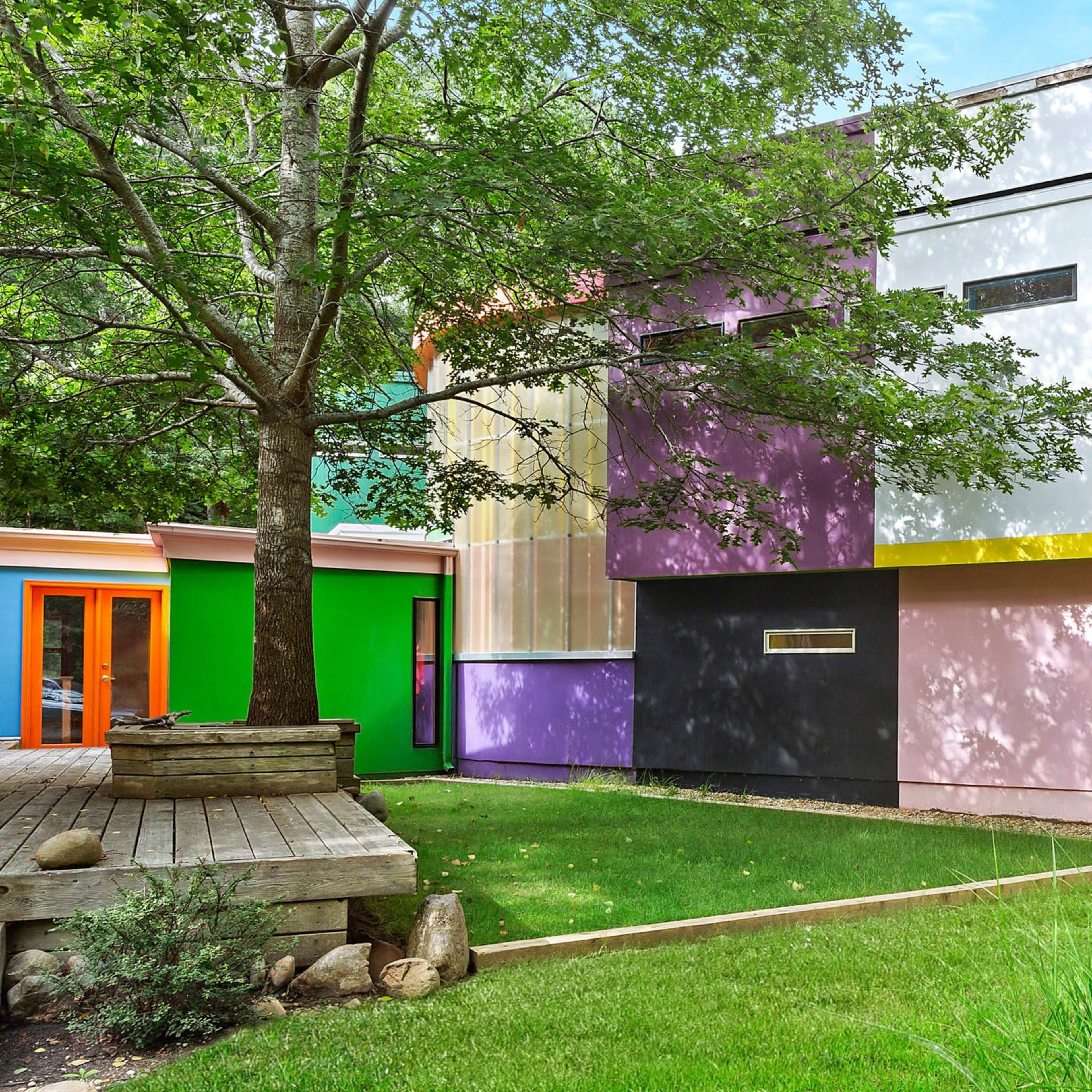 A modern house featuring geometric shapes and vibrant colors, surrounded by green grass and trees.