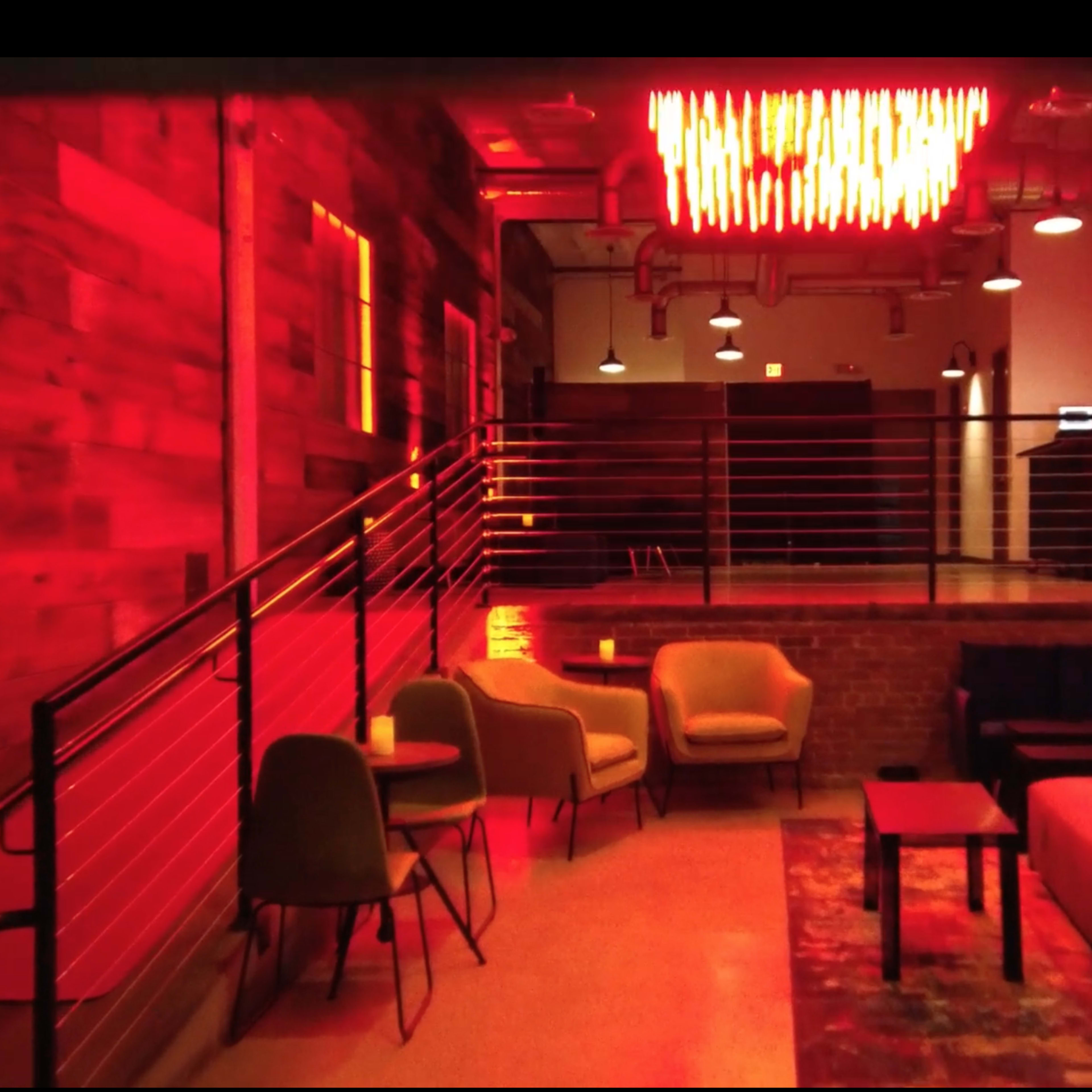The scene shows a modern lounge area with a mix of seating, wooden walls, and red lighting fixtures overhead.