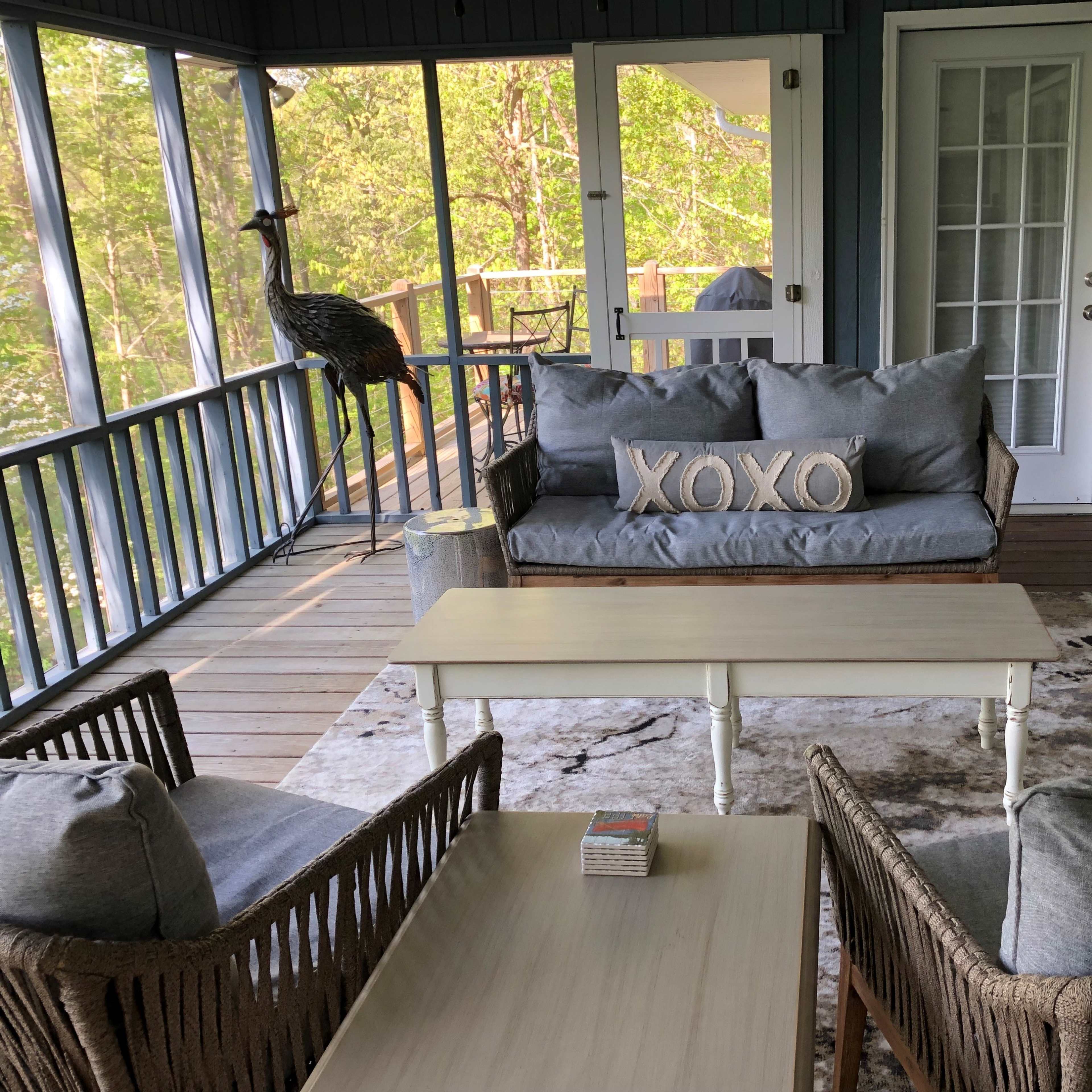 A screened-in porch with a gray sofa, two wicker chairs, and a small wooden coffee table, all arranged around a patterned rug.