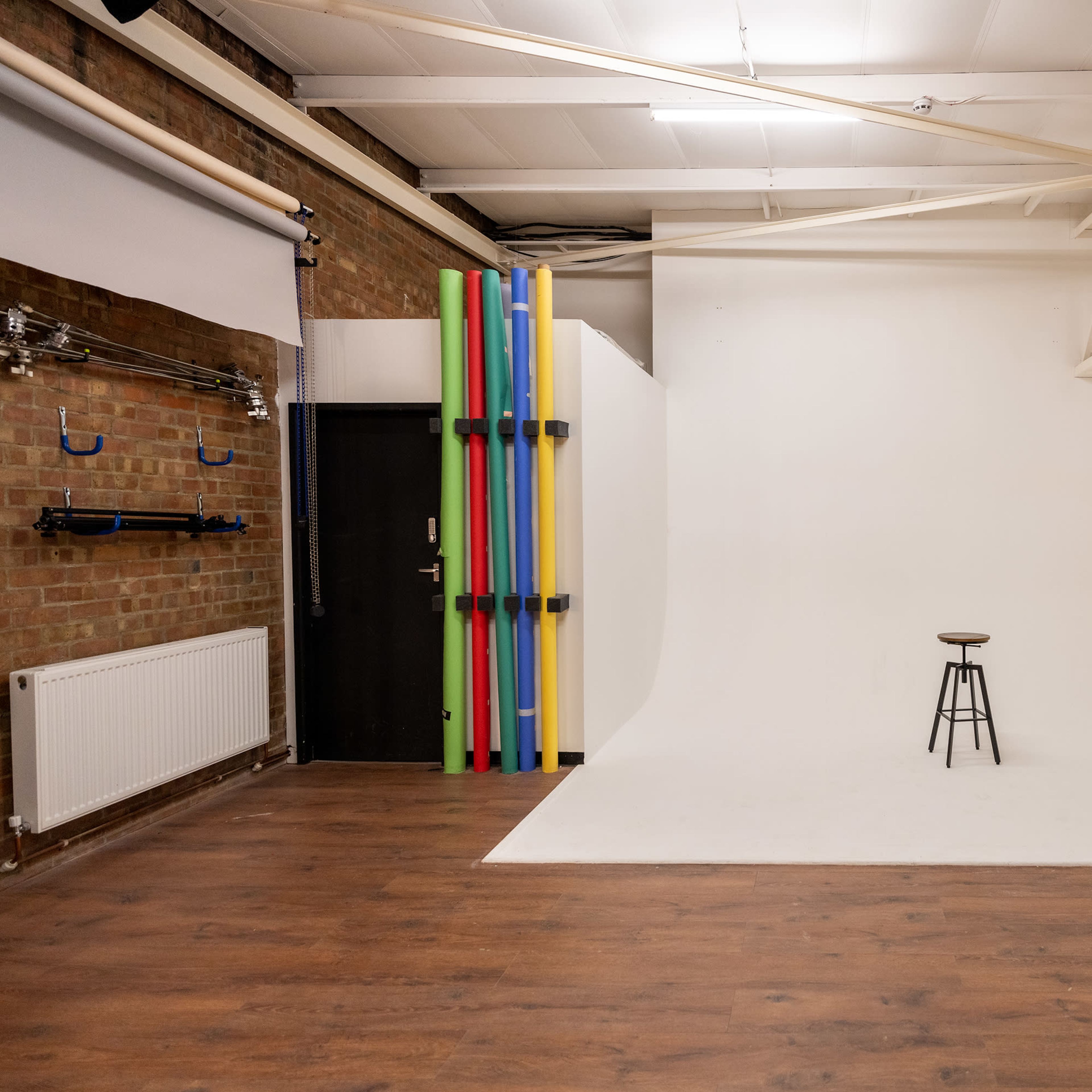 A spacious photography studio with a white backdrop, a wooden floor, and a single stool in the center.