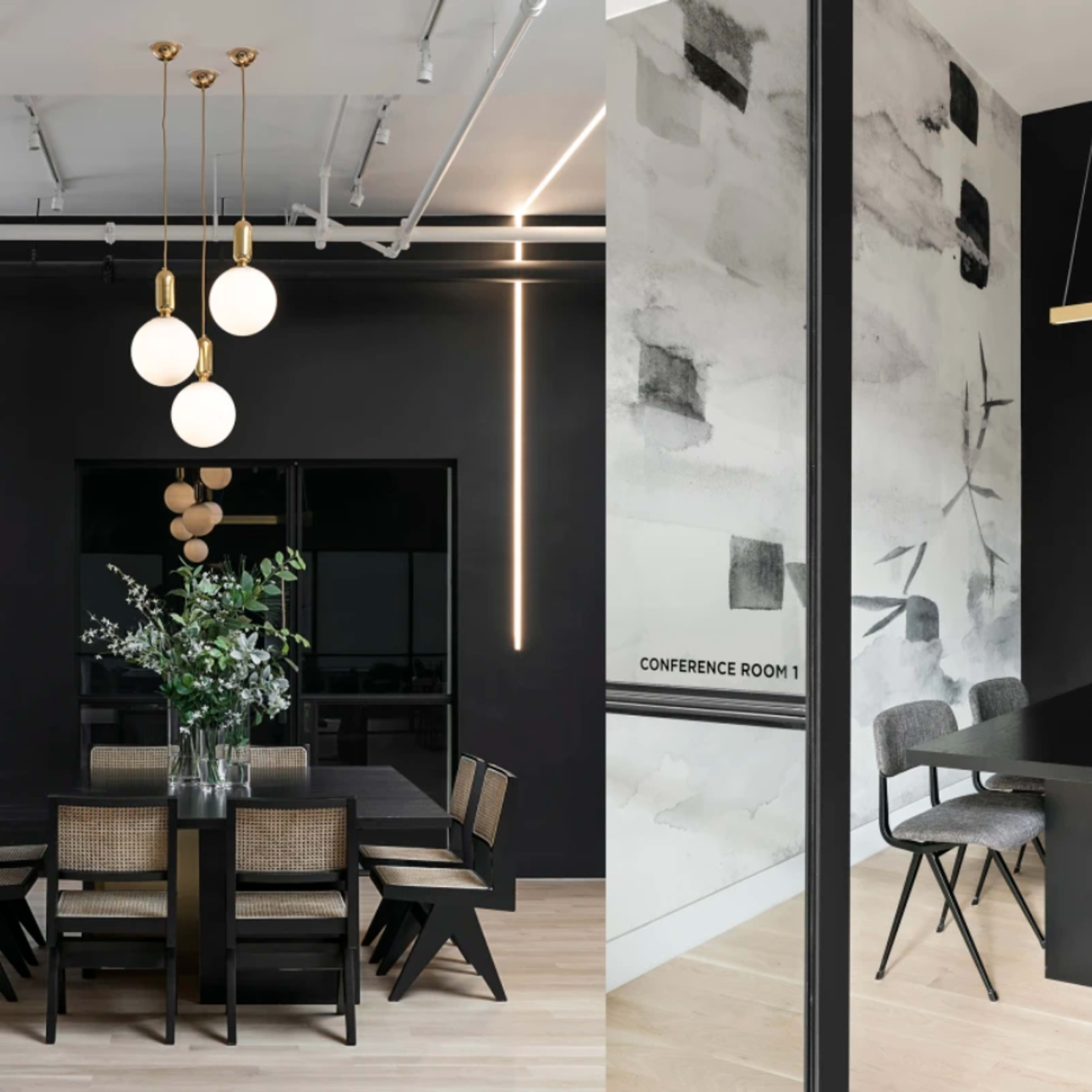 A modern dining area on the left with a dark table and chairs under pendant lights, and a conference room on the right featuring a long black table with chairs and a wall adorned with abstract art.