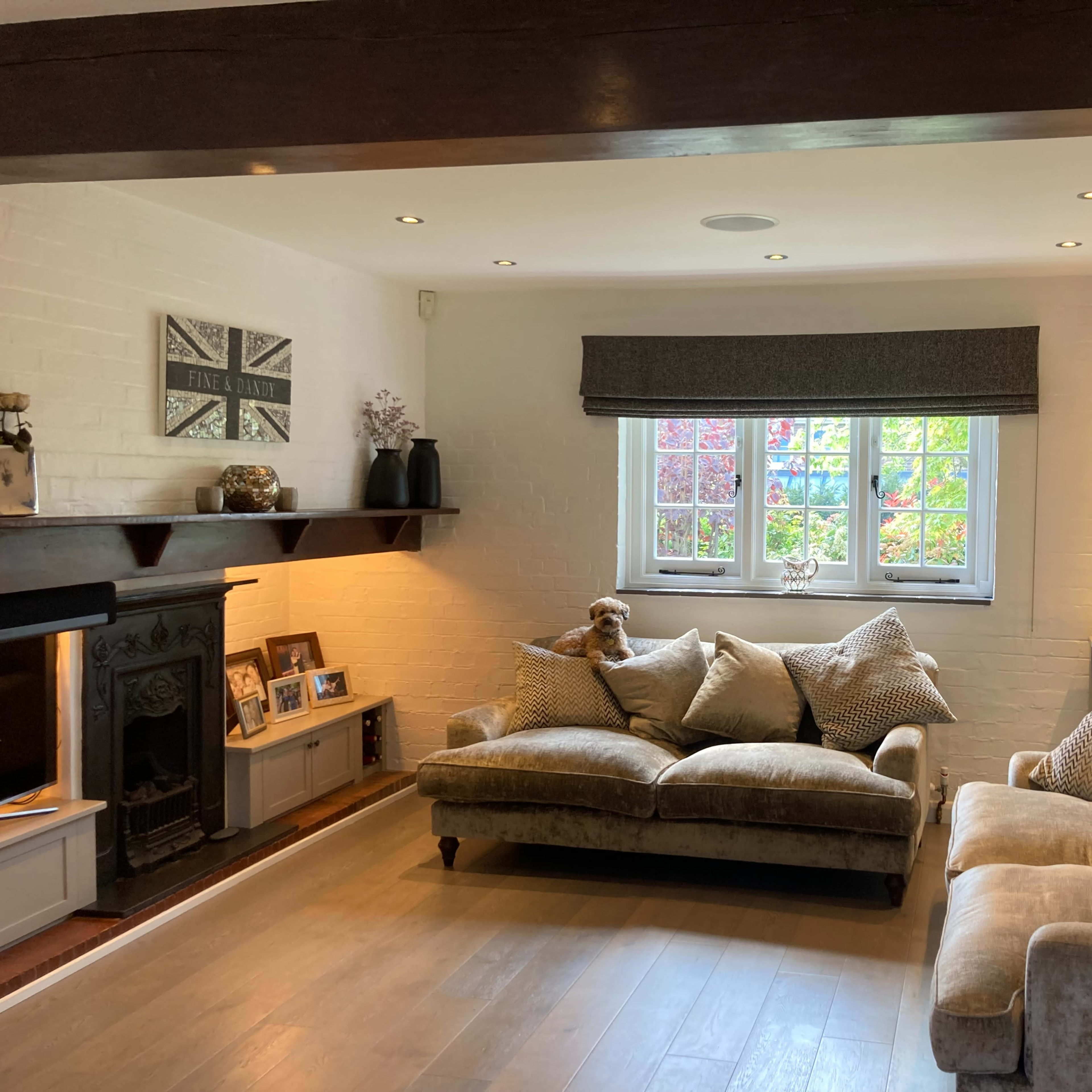 A living room with a comfortable beige sofa, a plush armchair, and a decorative wall with a fireplace and various framed pictures.
