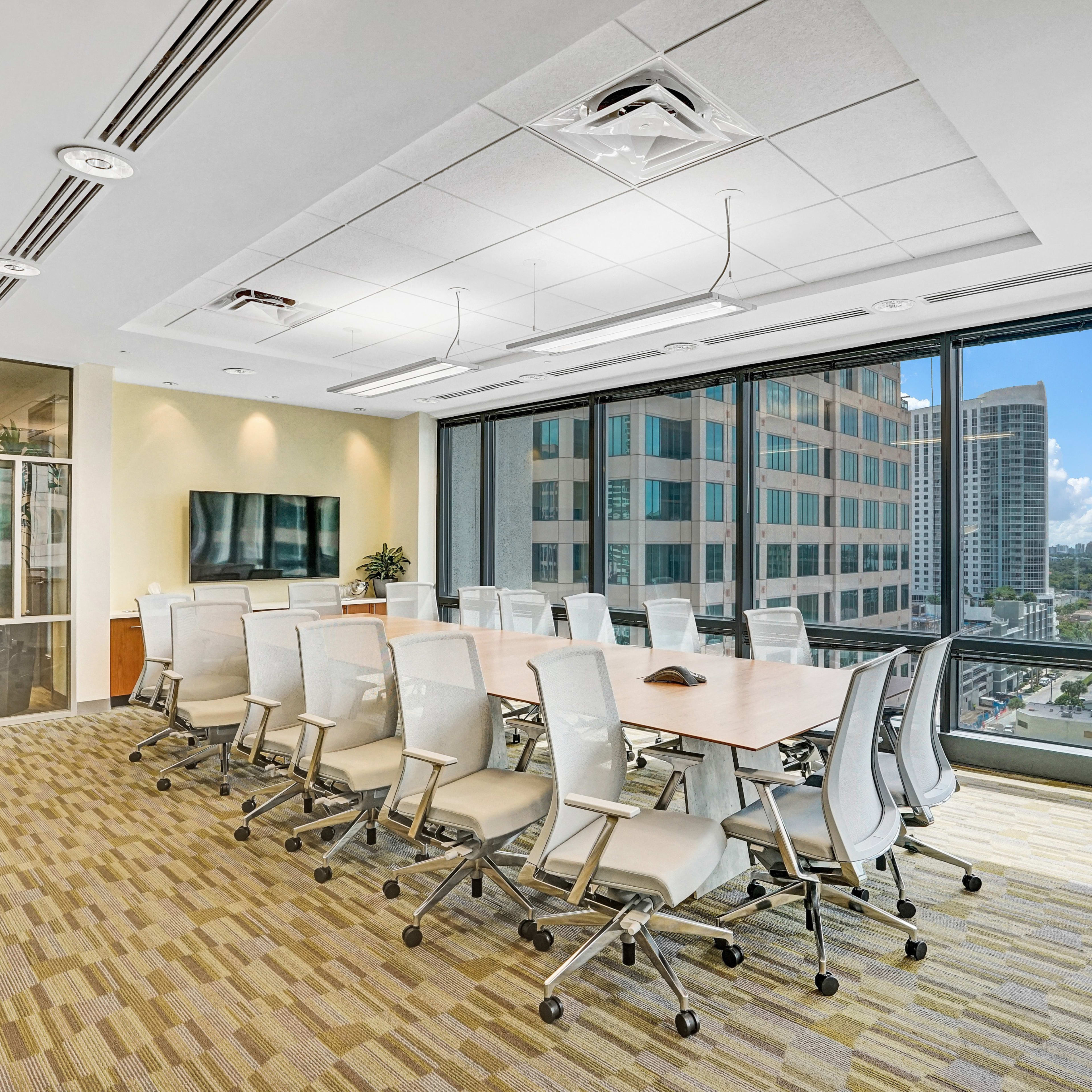 A modern conference room features a large table surrounded by ergonomic chairs, with floor-to-ceiling windows offering a view of the city skyline.