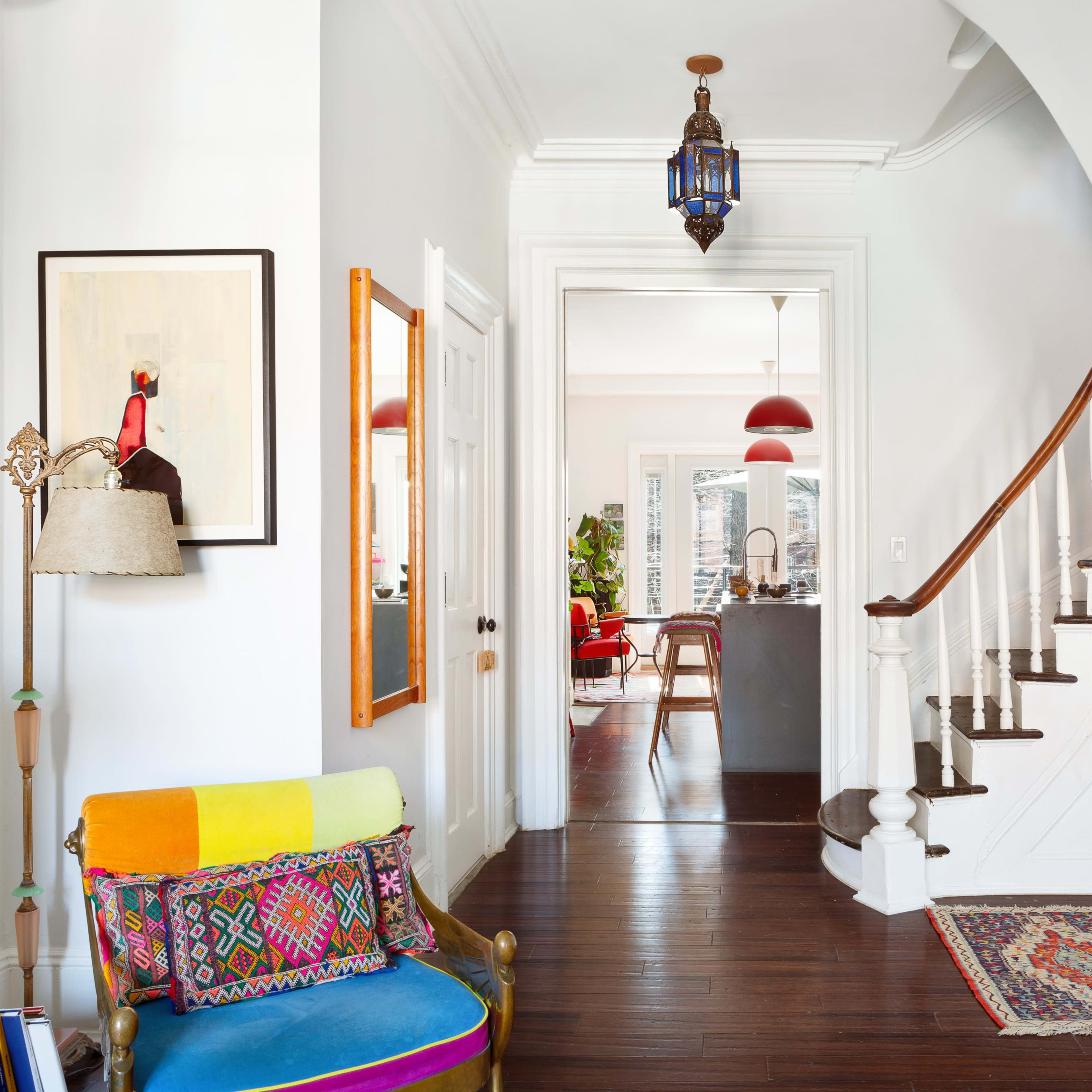 A modern entryway features a colorful seating area, a staircase with wooden banisters, and an open view into a light-filled living space.