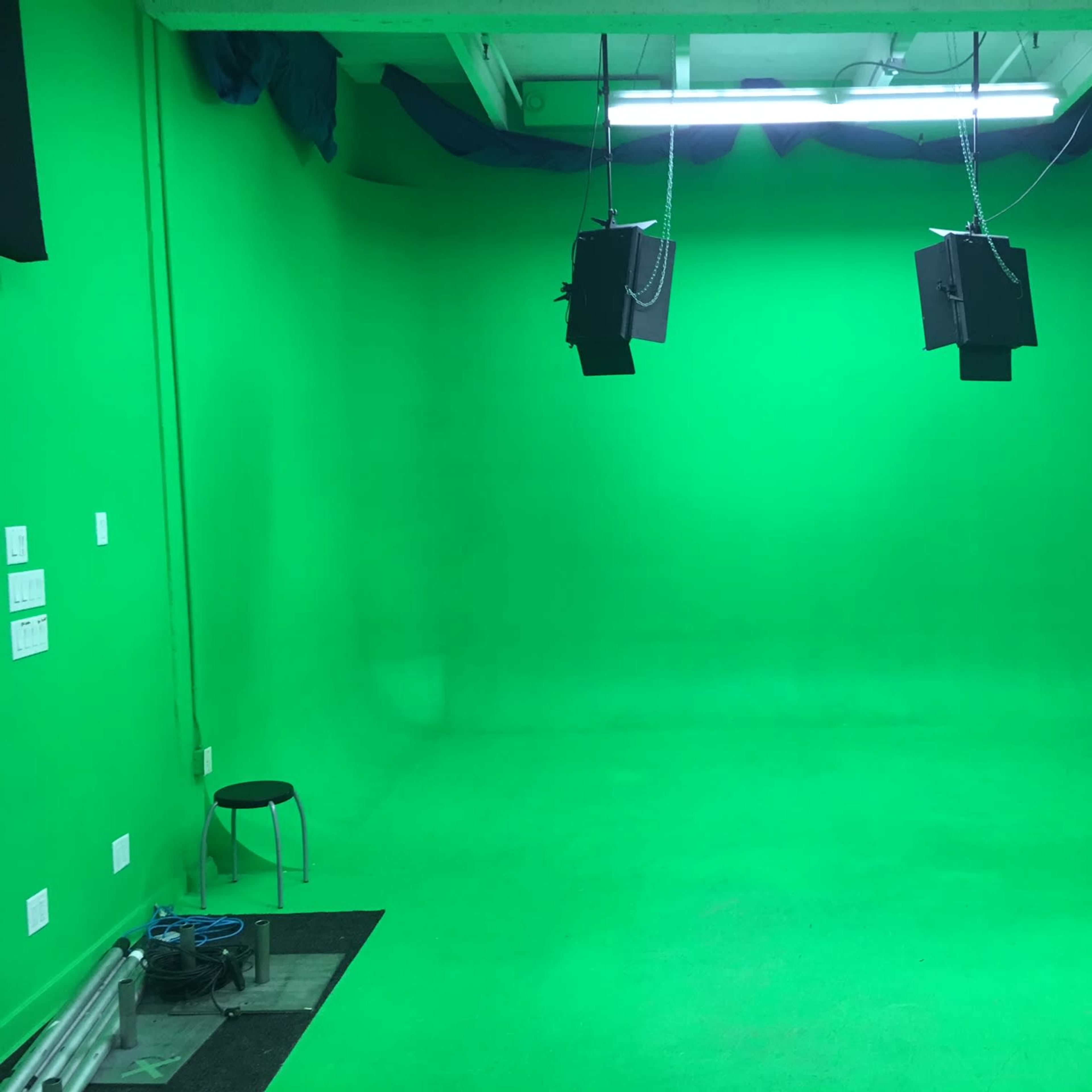 A green screen studio with two overhead lights and a solitary stool.