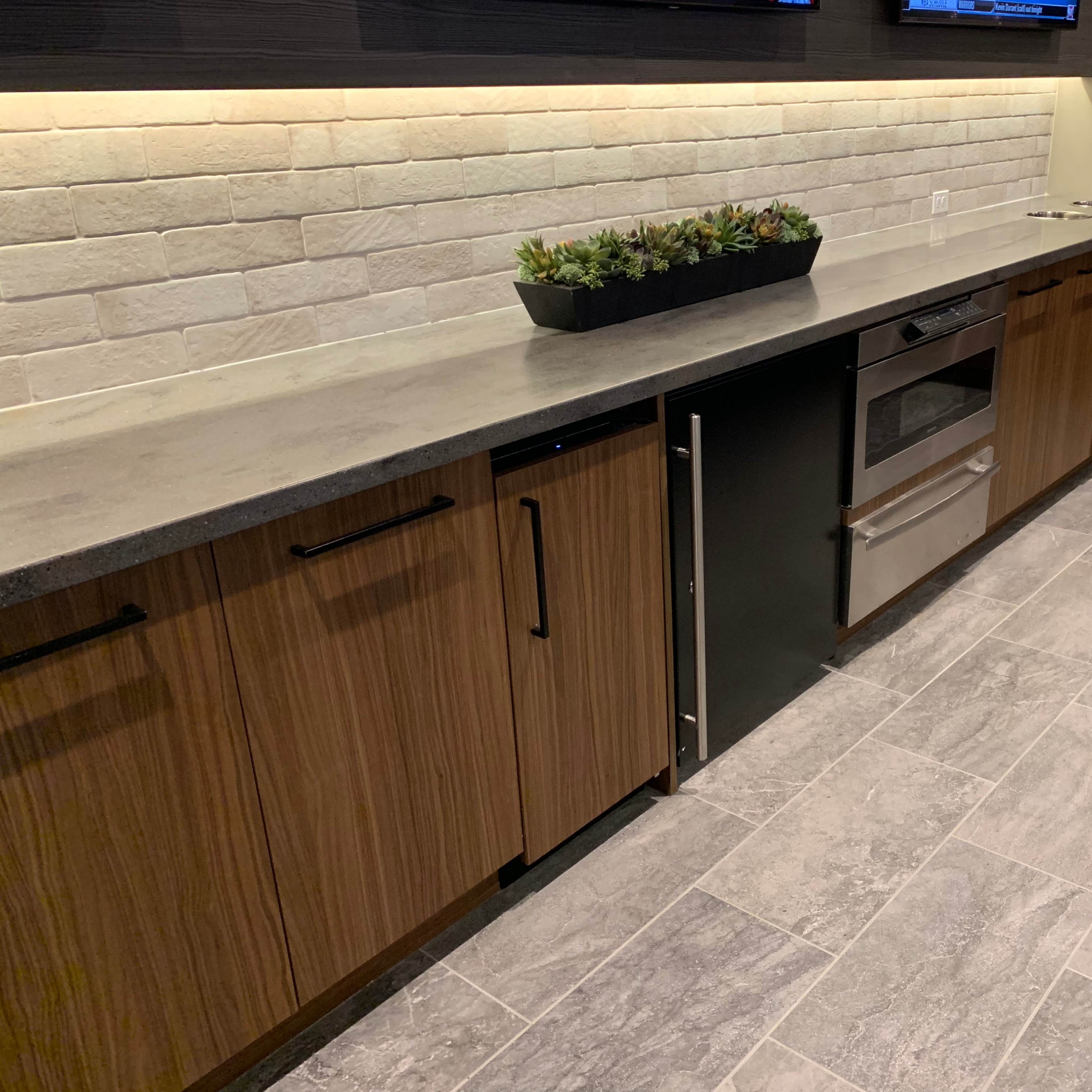 A modern kitchen with wooden cabinetry, a gray countertop, a built-in oven, and a row of small plants in a planter.