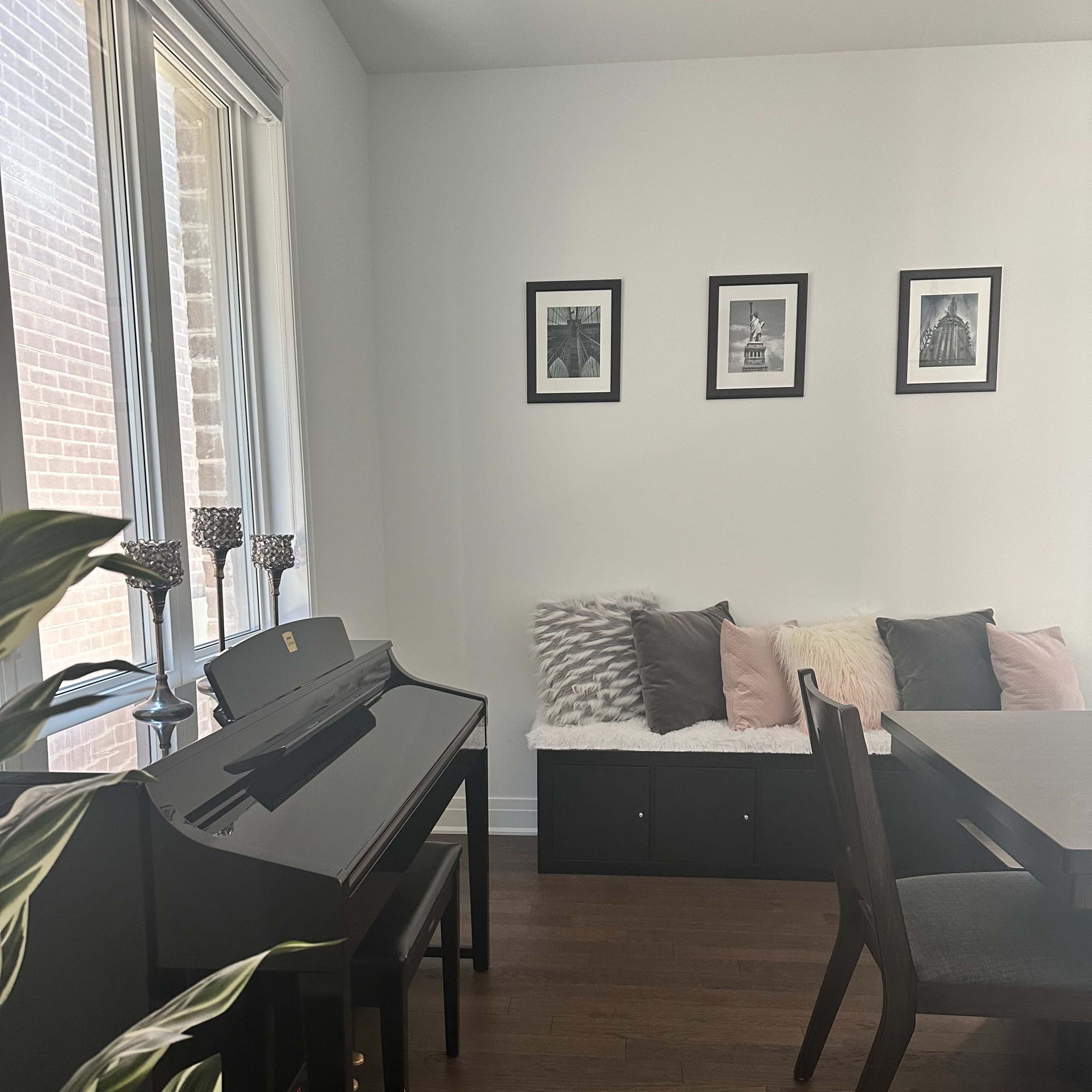 A black piano with two chairs is positioned beside a sofa adorned with pillows and framed photographs on the wall.