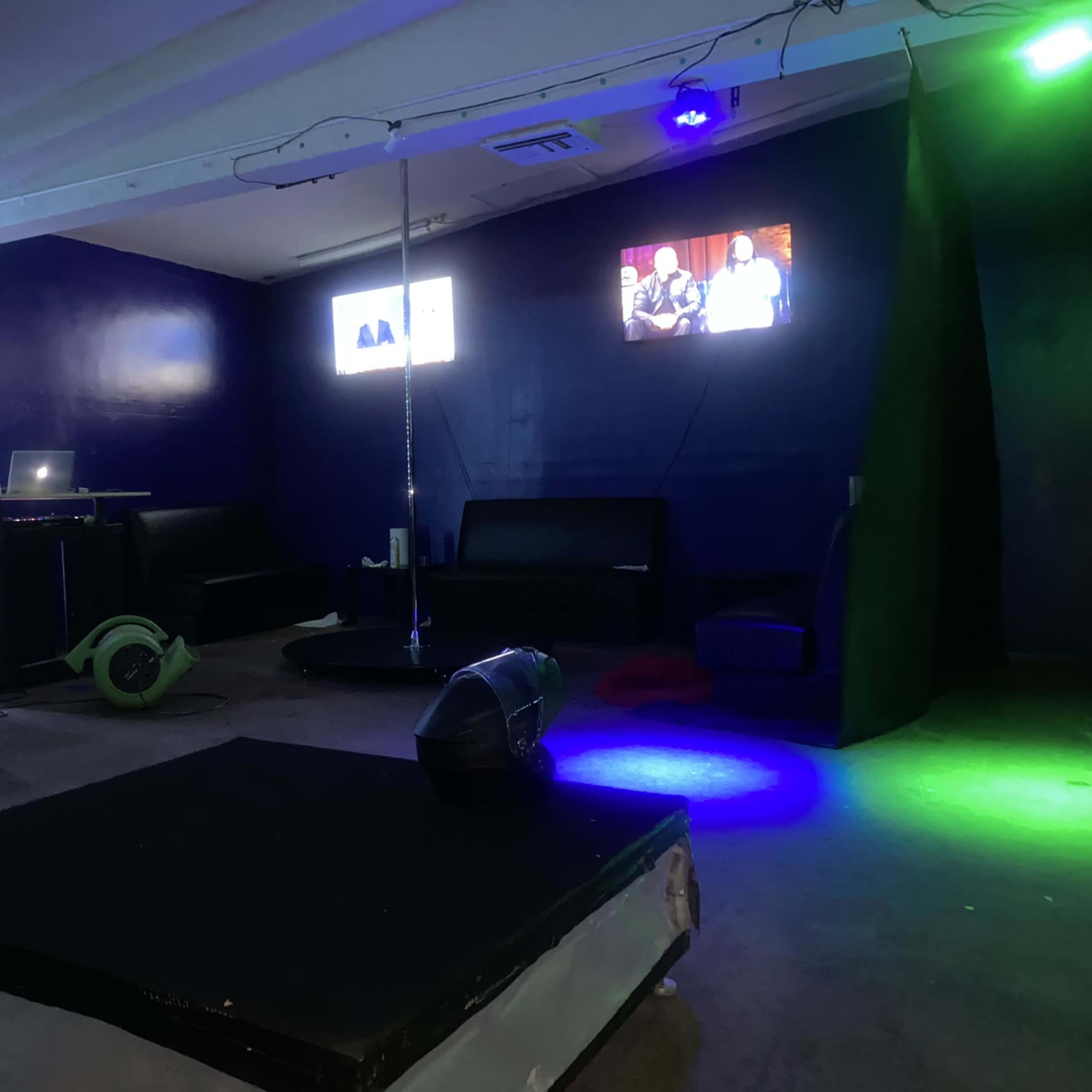 An indoor space with a small stage area, lighting effects, a DJ booth, and seating arrangements.