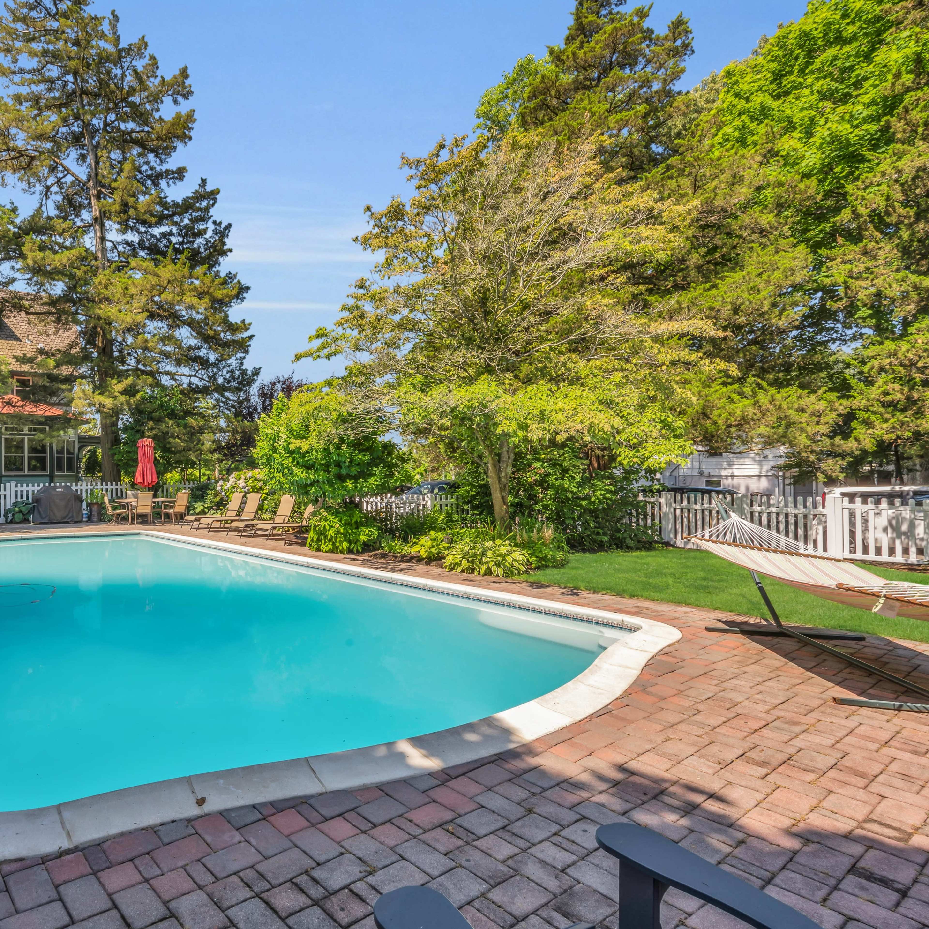 A residential backyard with a swimming pool surrounded by lounge chairs and lush greenery.